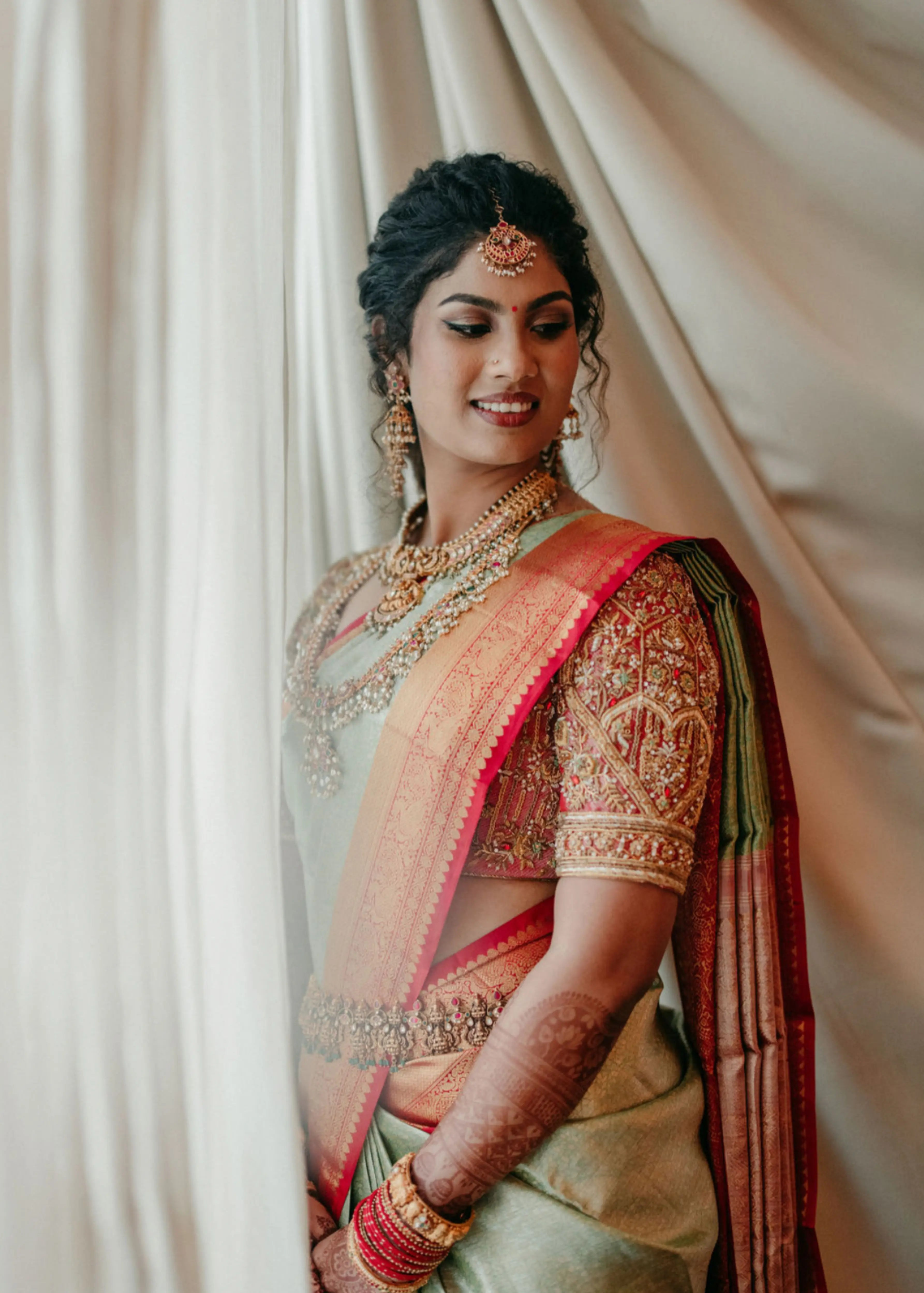 Bride in a concept red silk blouse handcrafted intricately with rhinestones, pearls, zardozi, resham knot work and stones, designed by Archana Karthick