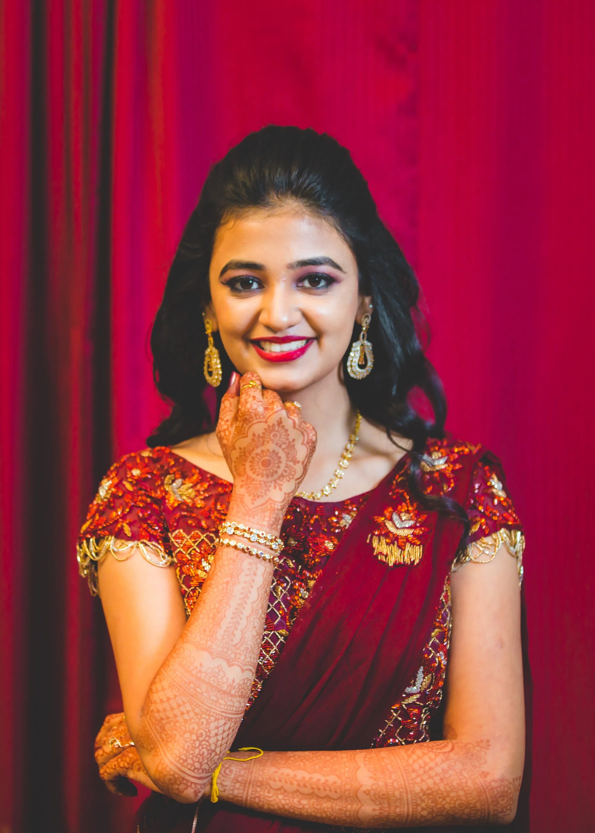 Bride from Chennai looking at camera and smiling in a handcrafted maroon raw silk gown with draped dupatta.