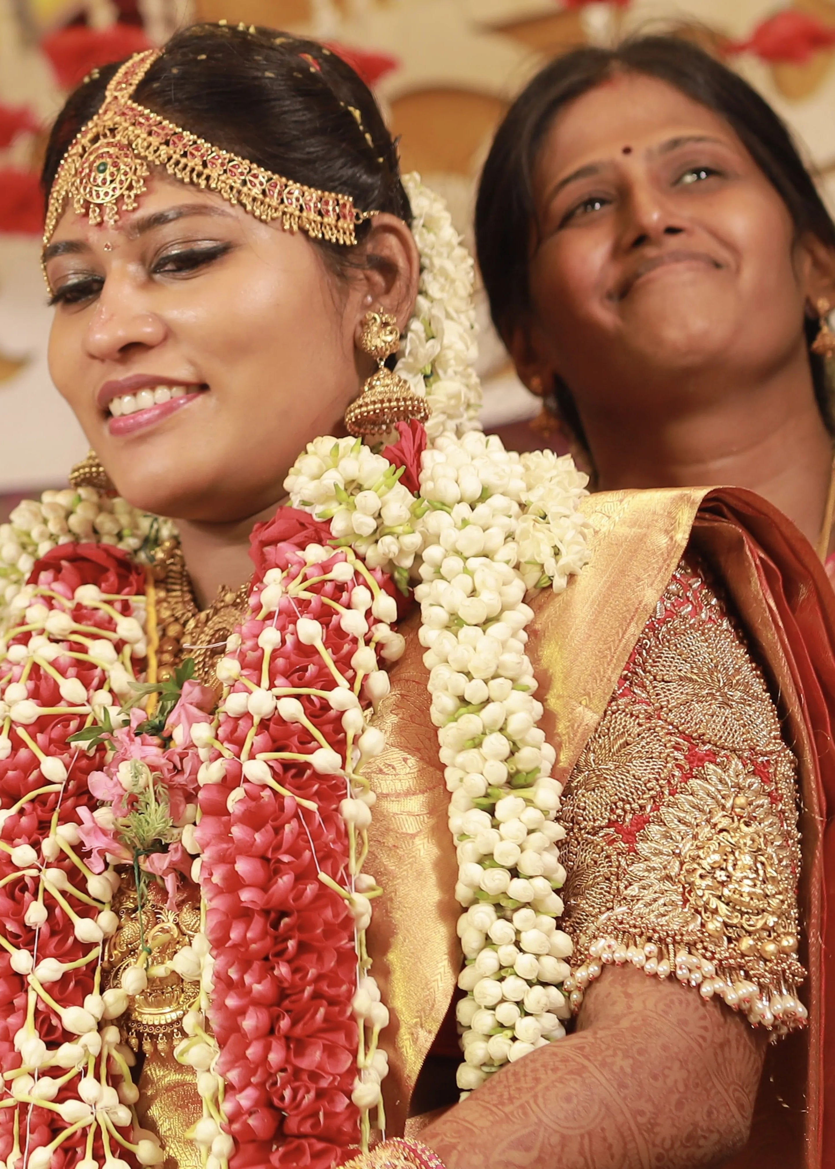 Bride from Chennai looking down in a handcrafted red raw silk blouse embellished with zardozi, pearls, beads with goddess pendants on sleeves.