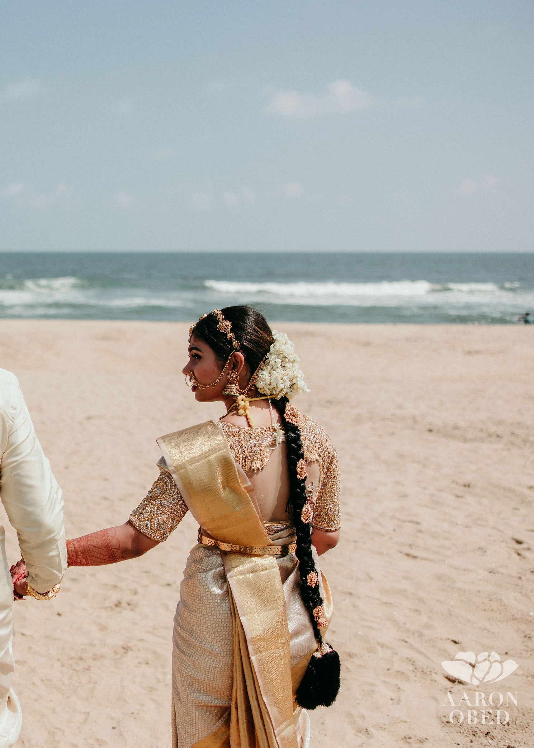 Bride from Chennai posing at beach with groom in a concept blouse in gold silk handcrafted intricately with zardozi, crystal beads, stones, pearls and beads. Designed by Archana Karthick.