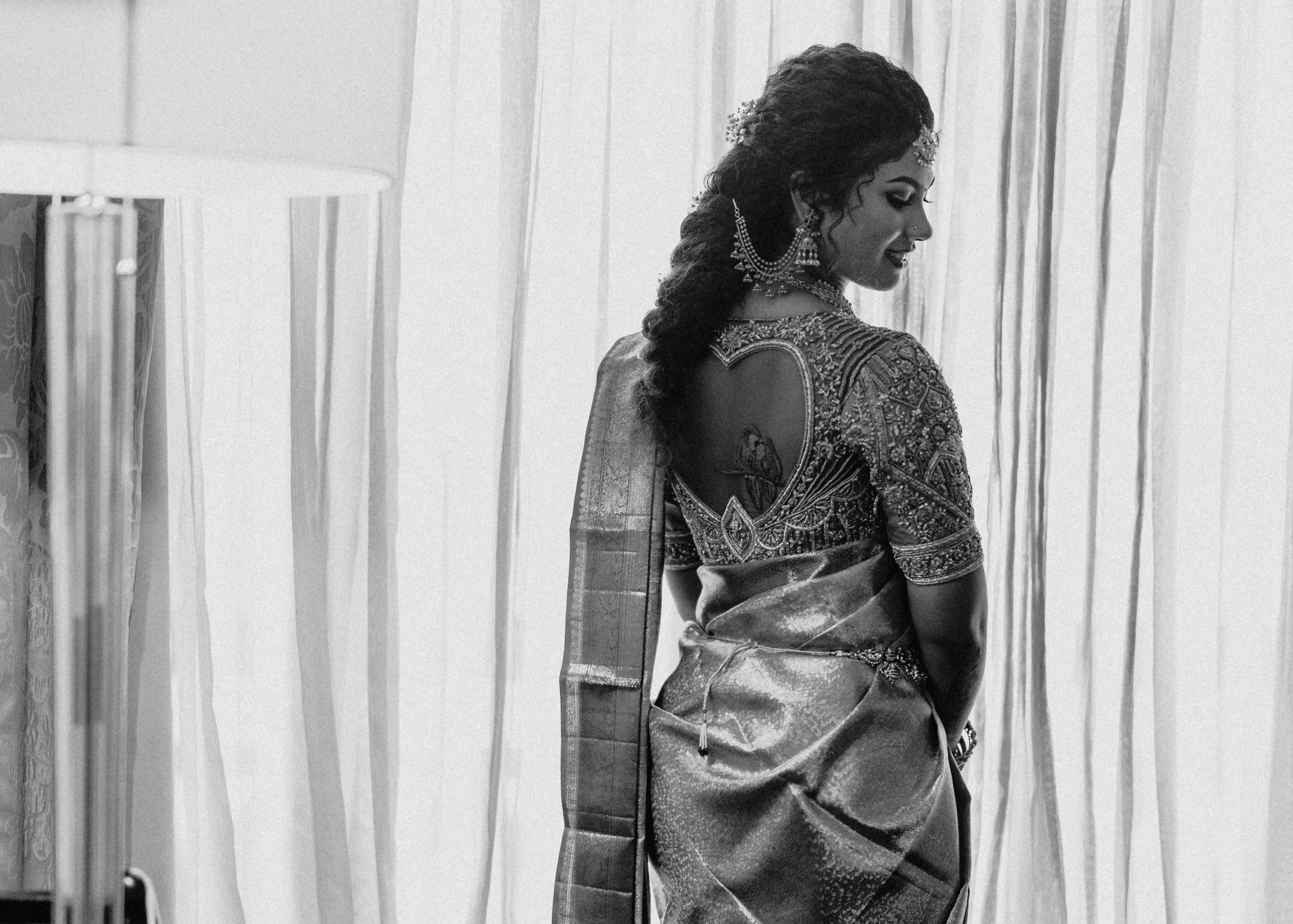 Bride from Chennai posing for blouse back design in a concept red silk blouse handcrafted intricately with rhinestones, pearls, zardozi, resham knot work and stones. Designed by Archana Karthick