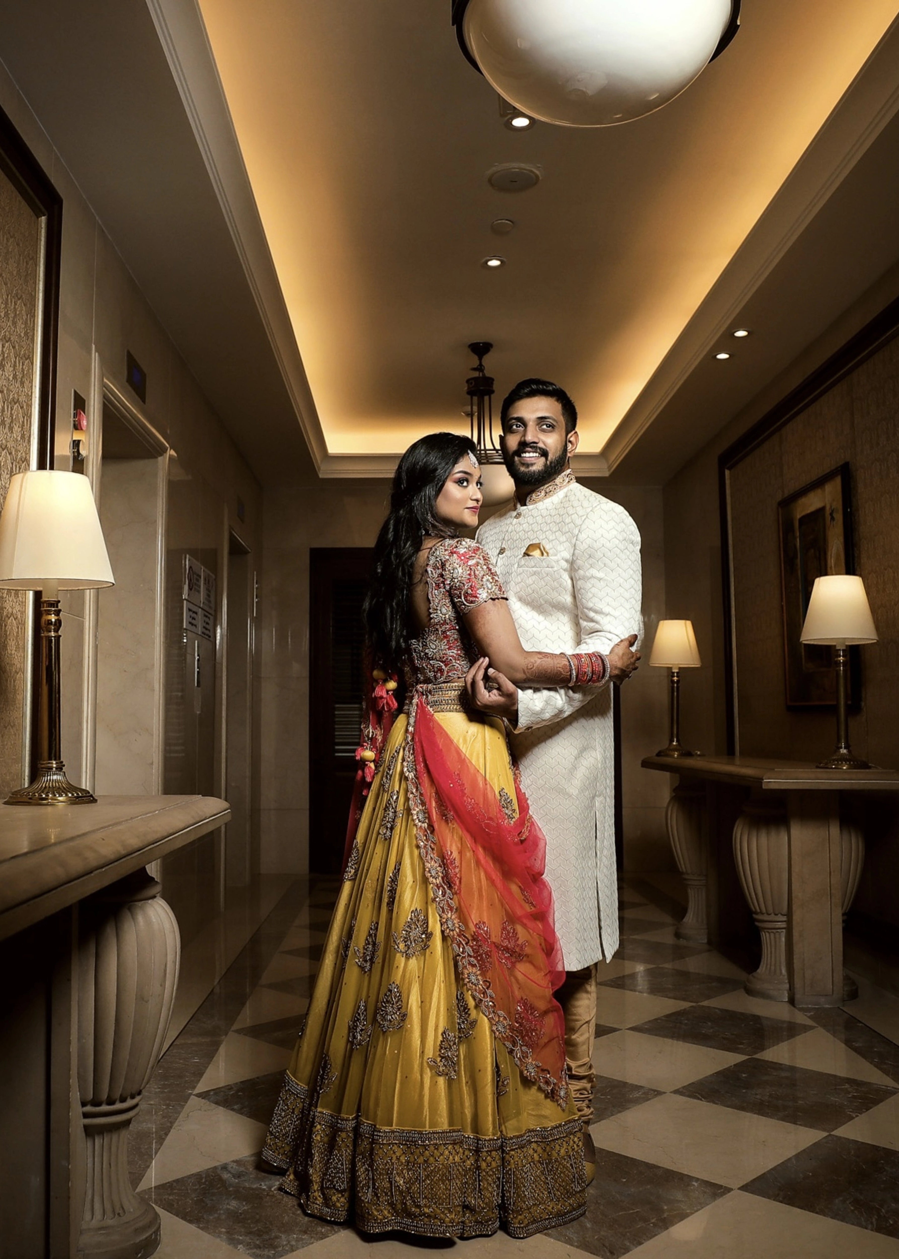 Bride from Chennai posing with groom in a yellow tulle skirt and dupatta and red raw silk blouse which make up the lehenga handcrafted intricately. Designed by Archana Karthick.