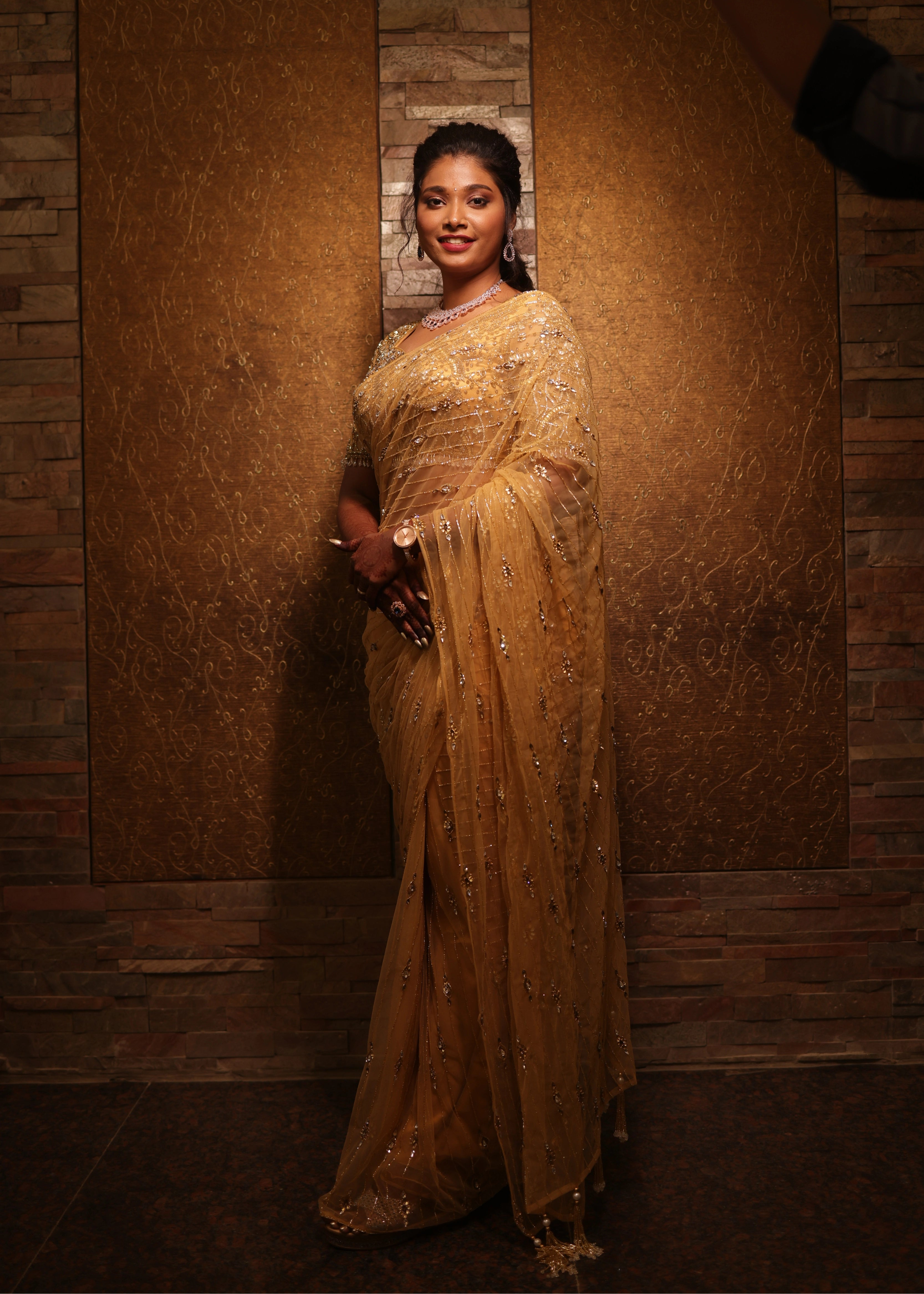 Bride from Chennai smiling at lens in a handcrafted metallic gold net saree designed by Archana Karthick with rhinestones