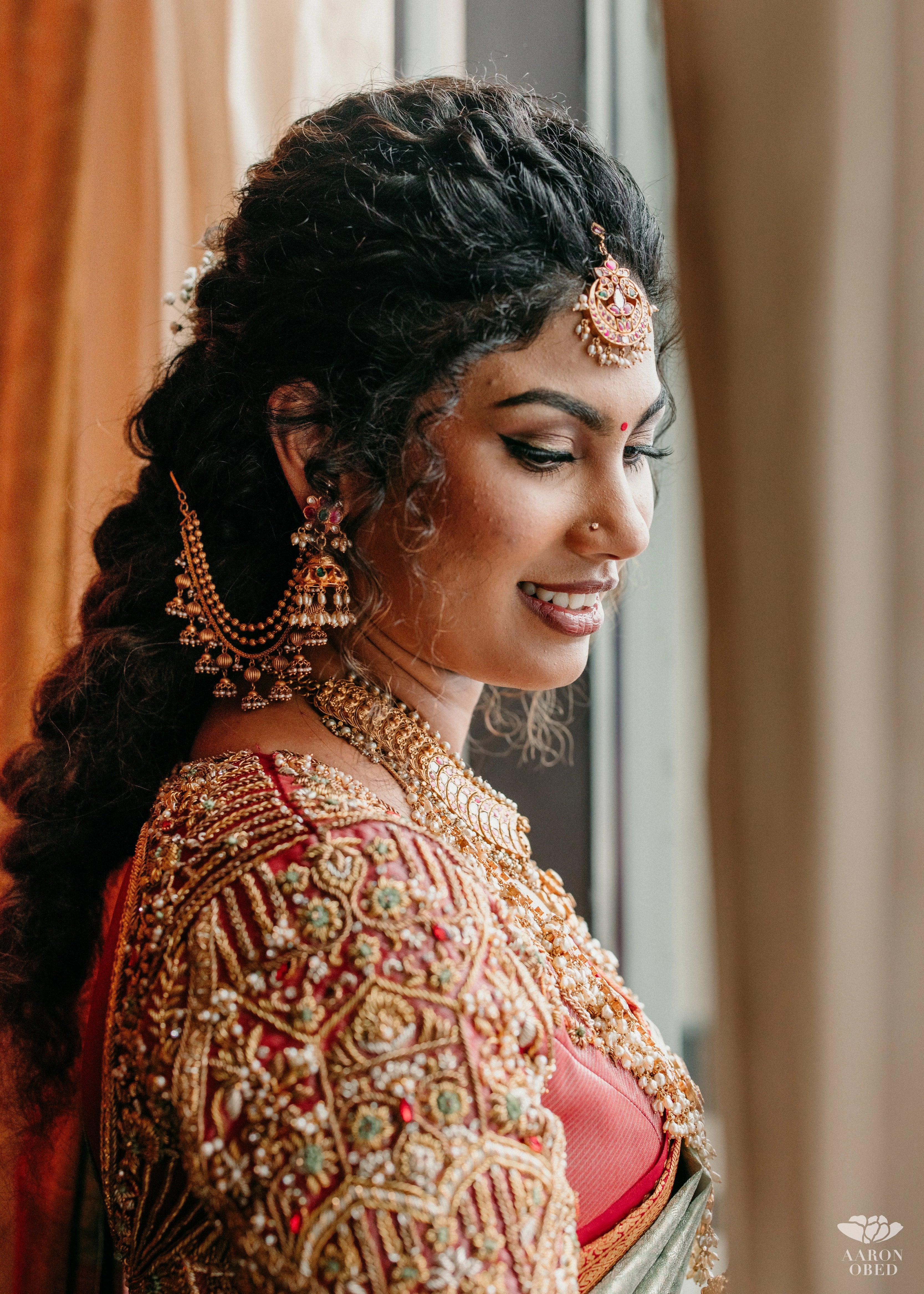 Bride from Chennai smiling in a concept red silk blouse handcrafted intricately with rhinestones, pearls, zardozi, resham knot work and stones. Designed by Archana Karthick