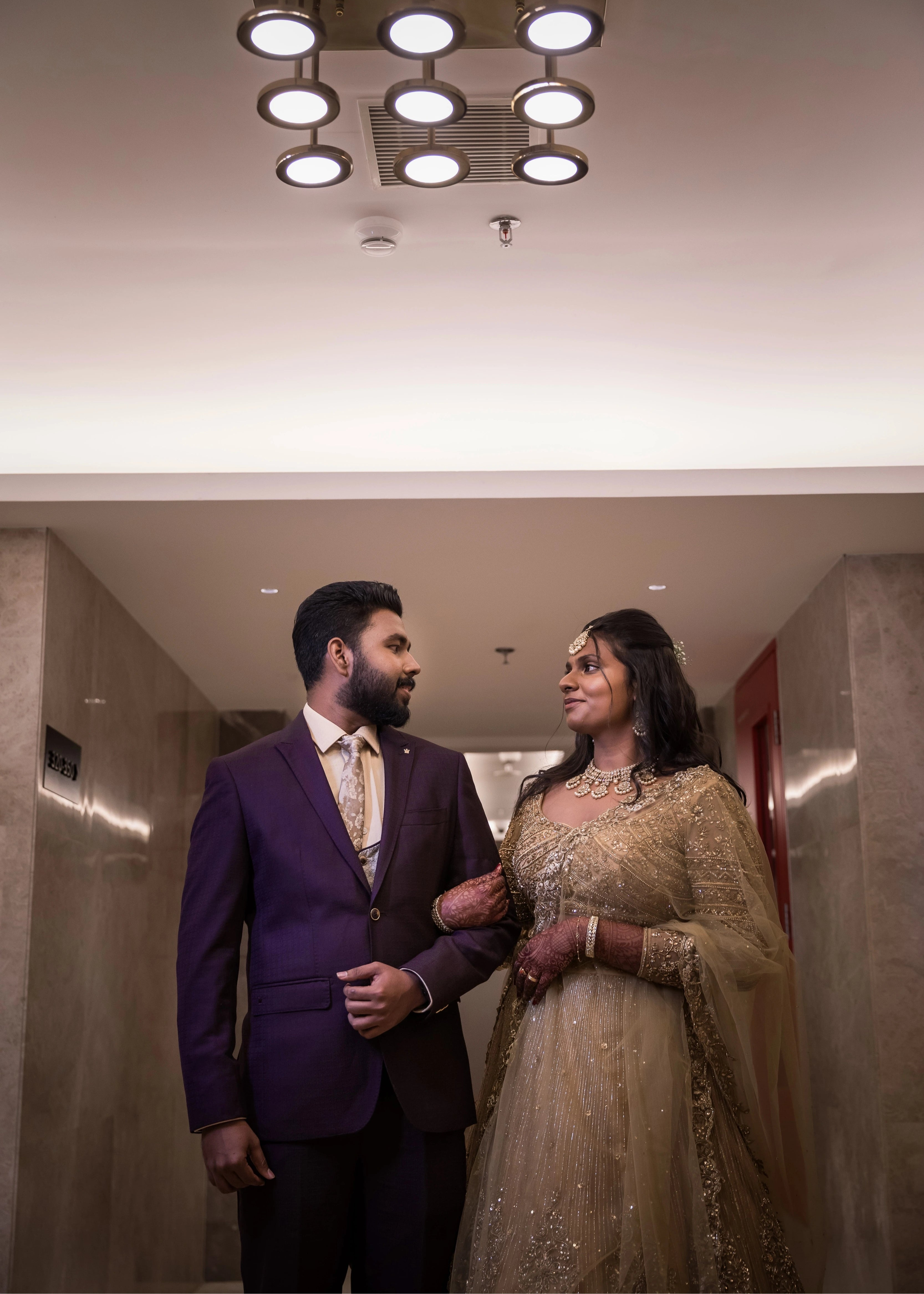 Bride from Singapore posing with groom in a gold lehenga in tulle designed by Archana Karthick handcrafted intricately with rhinestones, crystal beads, cutdanas and sequins.