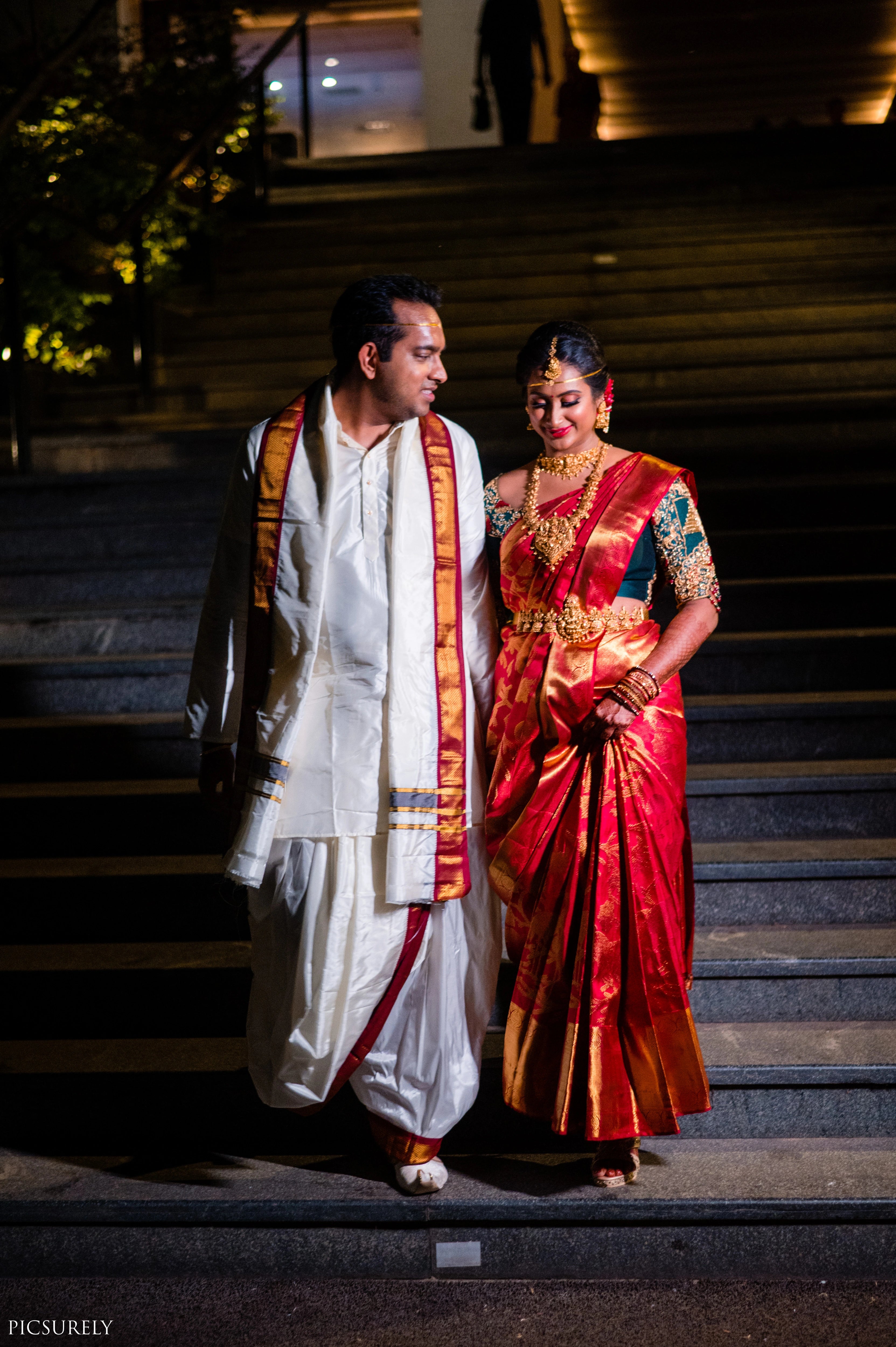 Bride from USA smiling with groom in a bottle green raw silk concept blouse for her wedding, handcrafted with zardozi, stones, beads, resham work and kundan by Archana Karthick.