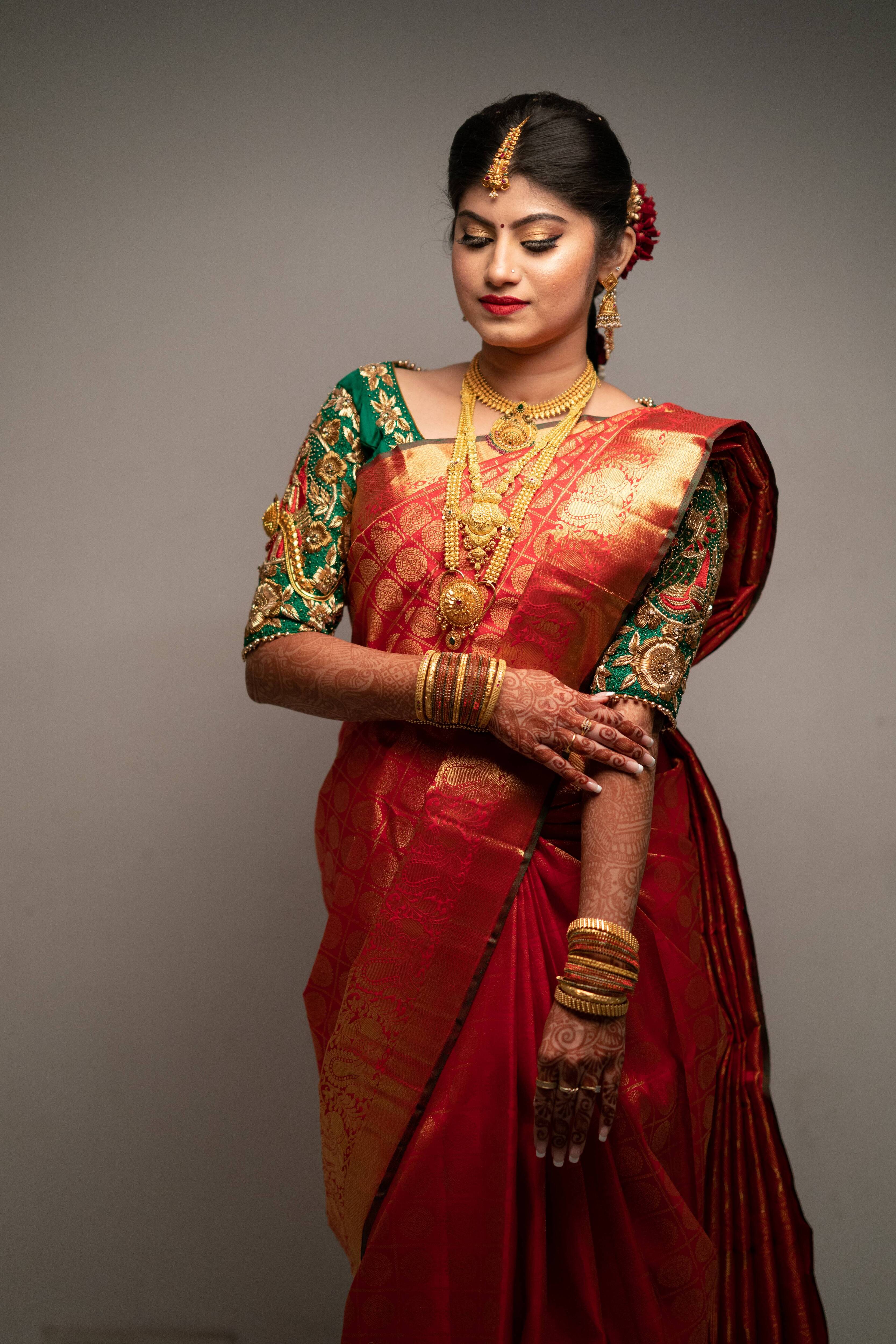 Bride Vandita is seen here in our Handcrafted Concept Bridal Blouse in Bottle Green Raw Silk. The bride is seen looking down with a smile while her left and right blouse sleeve embroidery designs are visible clearly.