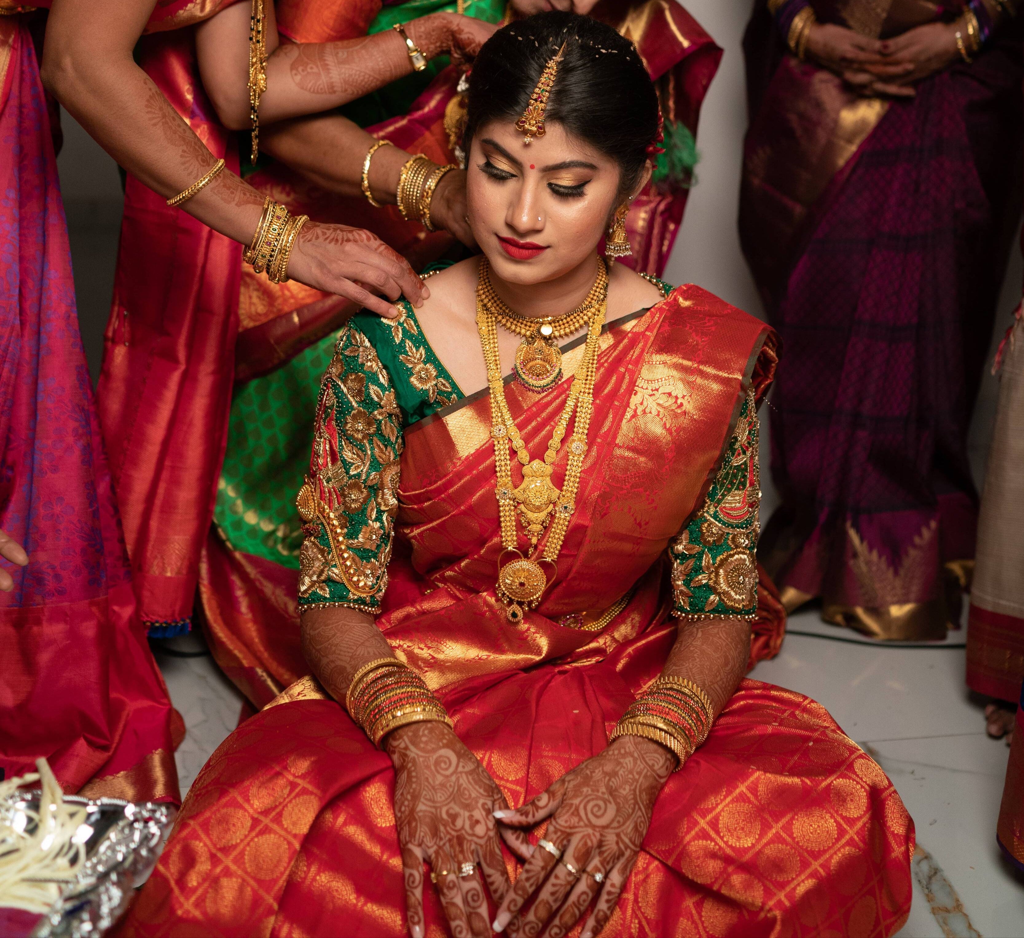Bride Vandita is seen here in our Handcrafted Concept Bridal Blouse in Bottle Green Raw Silk. The bride is seen being helped by her relatives and loved ones. Her left and right blouse sleeve embroidery designs are visible clearly from the front.