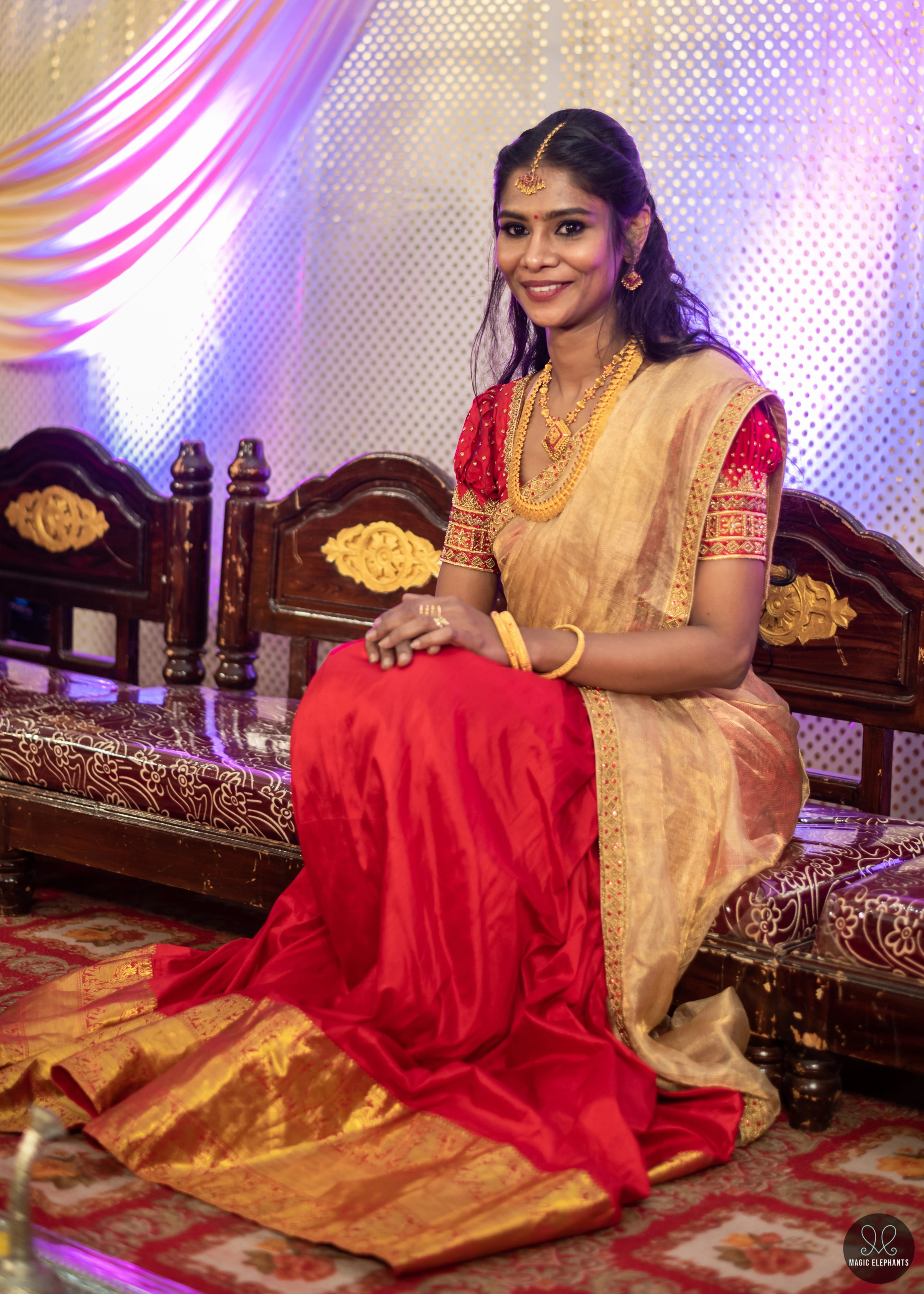 Bride seated in a handcrafted red silk half saree with katori cut blouse has intricate zardozi and stone work.