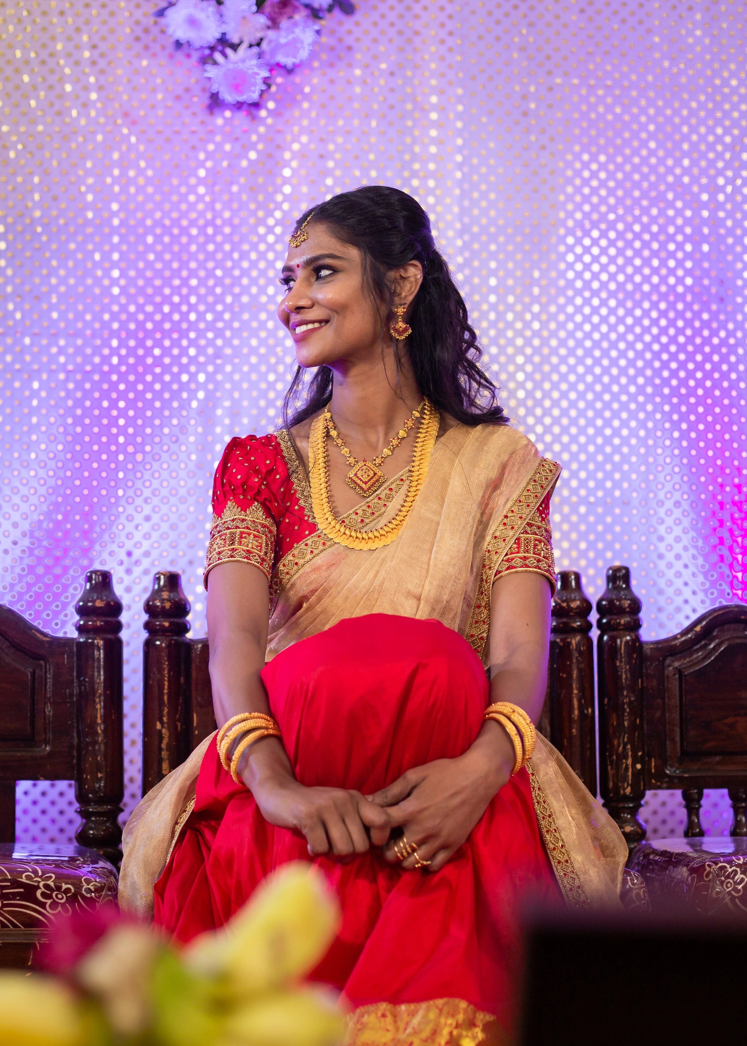Bride smiling in a handcrafted red silk half saree with katori cut blouse has intricate zardozi and stone work.