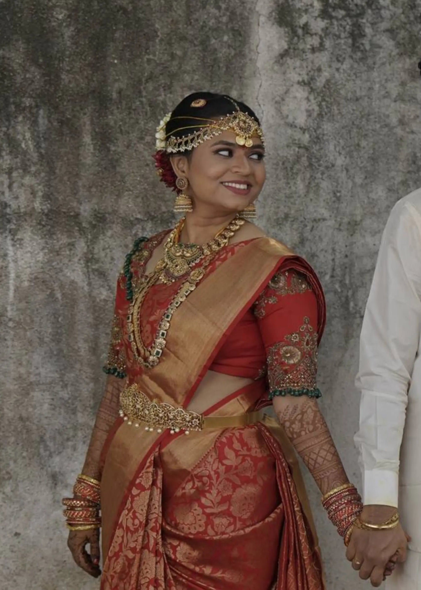 Bride smiling in red silk blouse handcrafted intricately with stones, beads, cutdanas and sequins. Designed by Archana Karthick