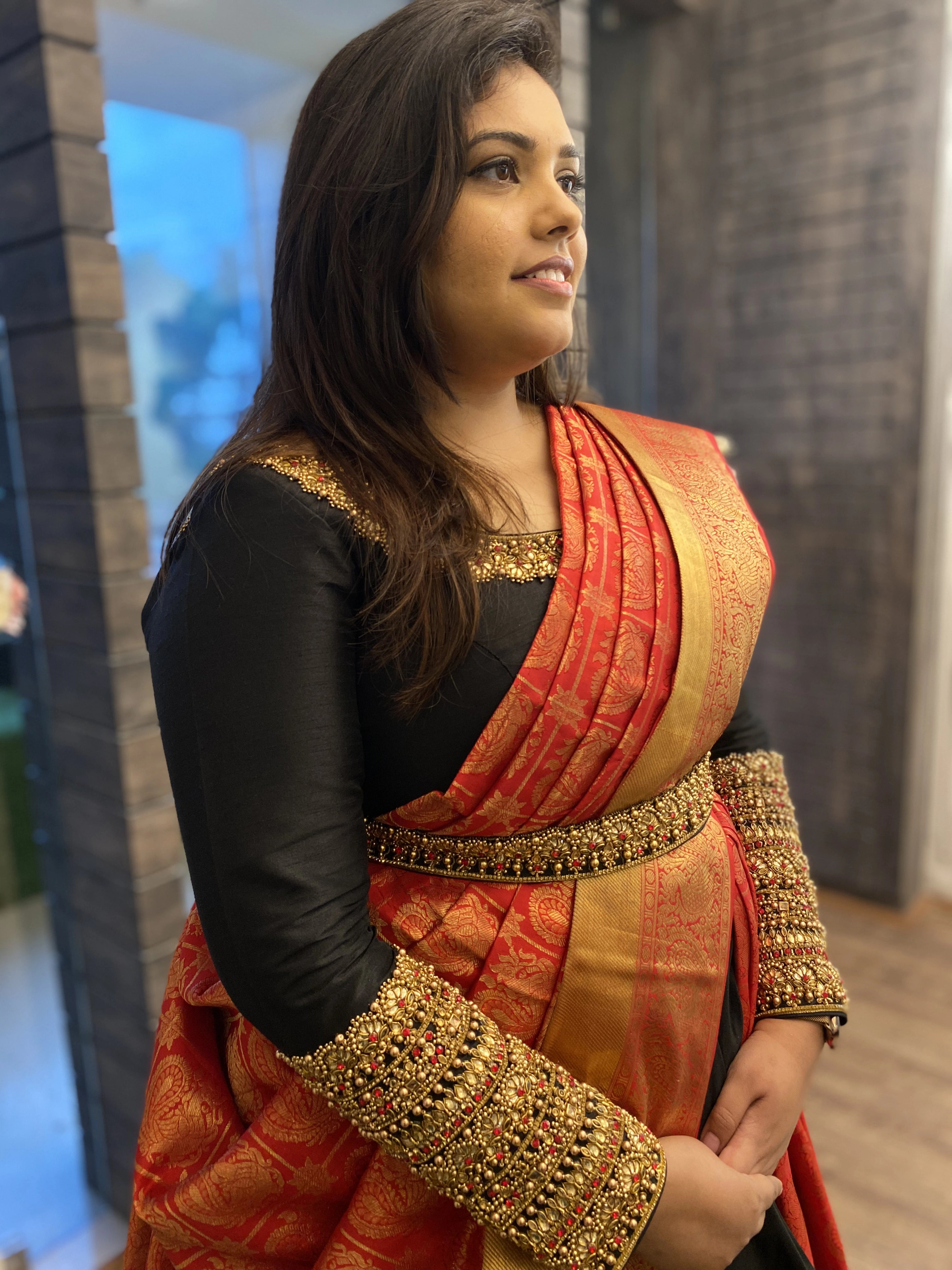Bridesmaid Nishitha showcasing side profile in a black and burnt orange half saree, handcrafted with kemp stones, sequins, beads, zardozi and kundan by team Archana Karthick.