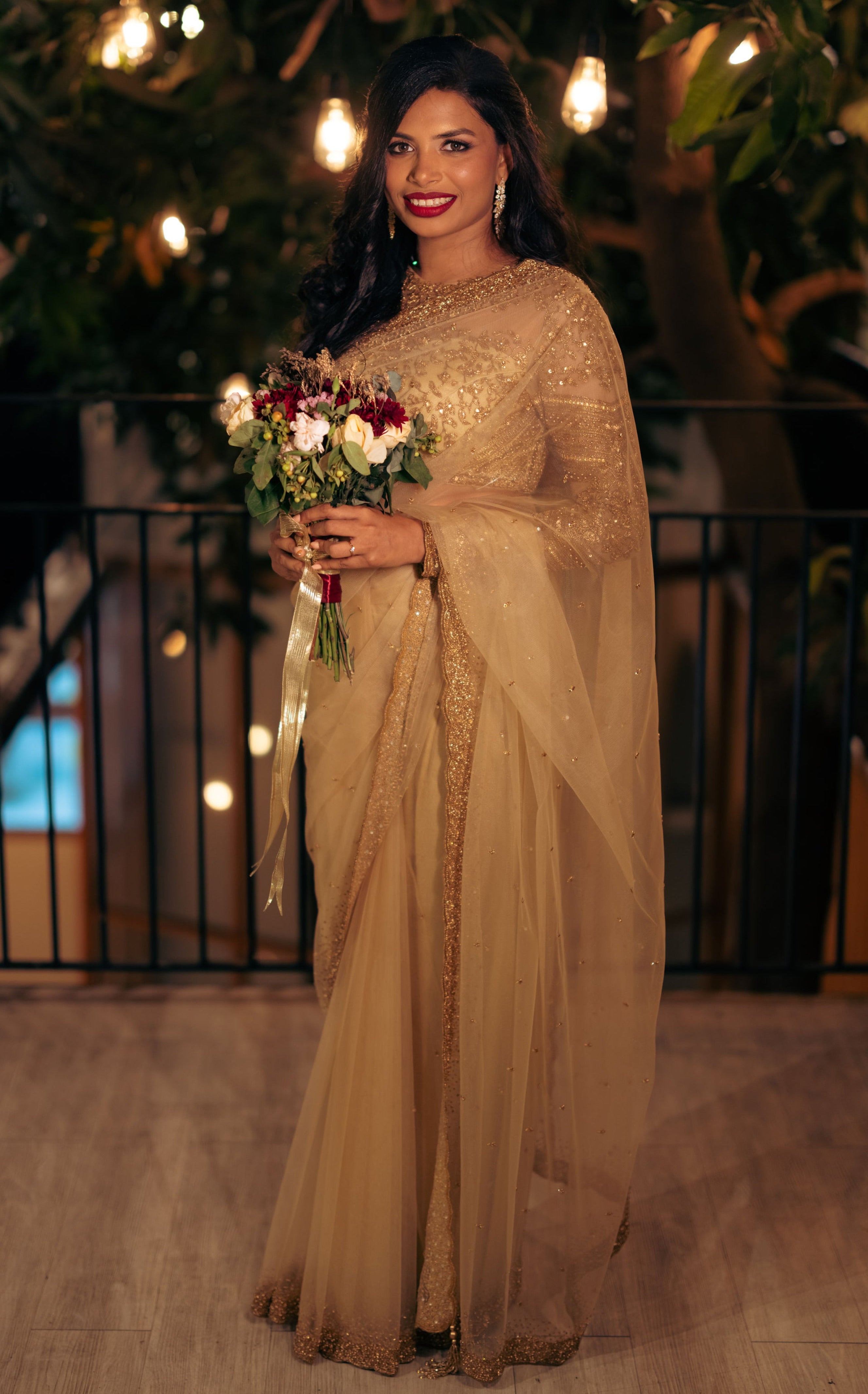 Christian Bride Steffi in handcrafted net saree in champagne gold designed by Archana Karthick. Posing for a full front profile with a bouquet in hand.