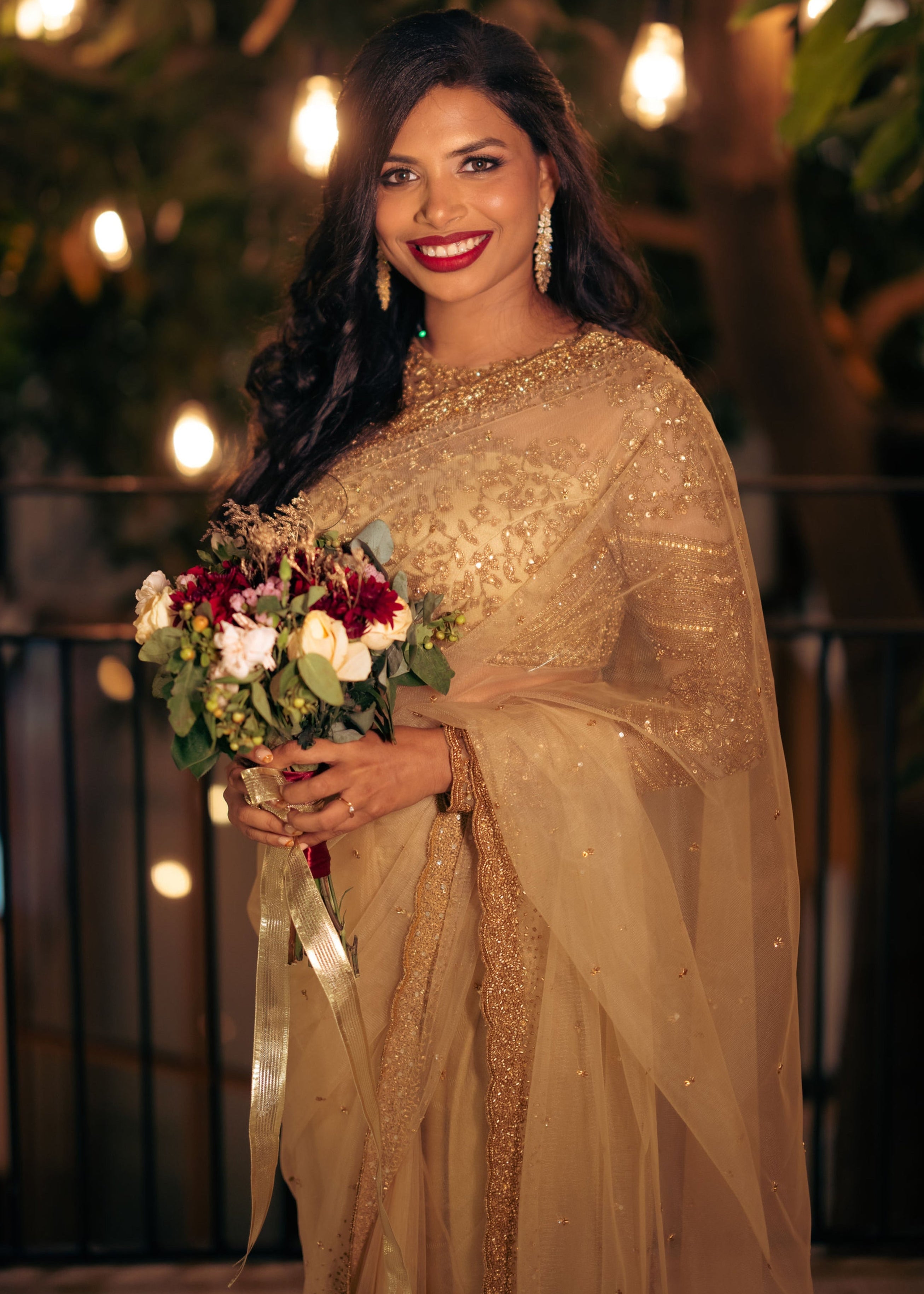 Christian Bride Steffi in handcrafted net saree in champagne gold designed by Archana Karthick. Posing with a bouquet in hand for a half front profile.