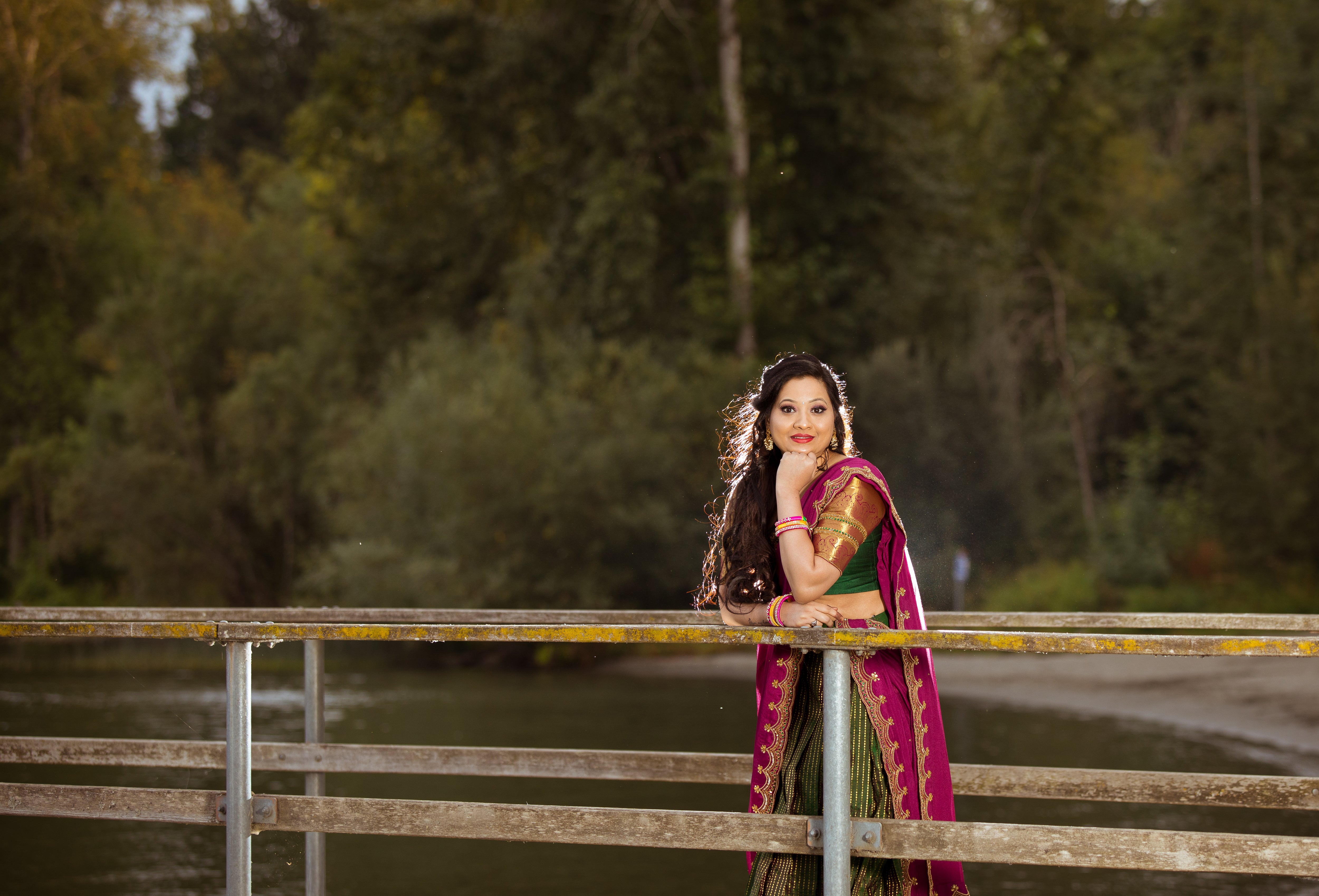 Client, Swathi Pillai, from Seattle leaning forward on a railing and posing in a bottle green and magenta silk traditional half saree designed by archana karthick.
