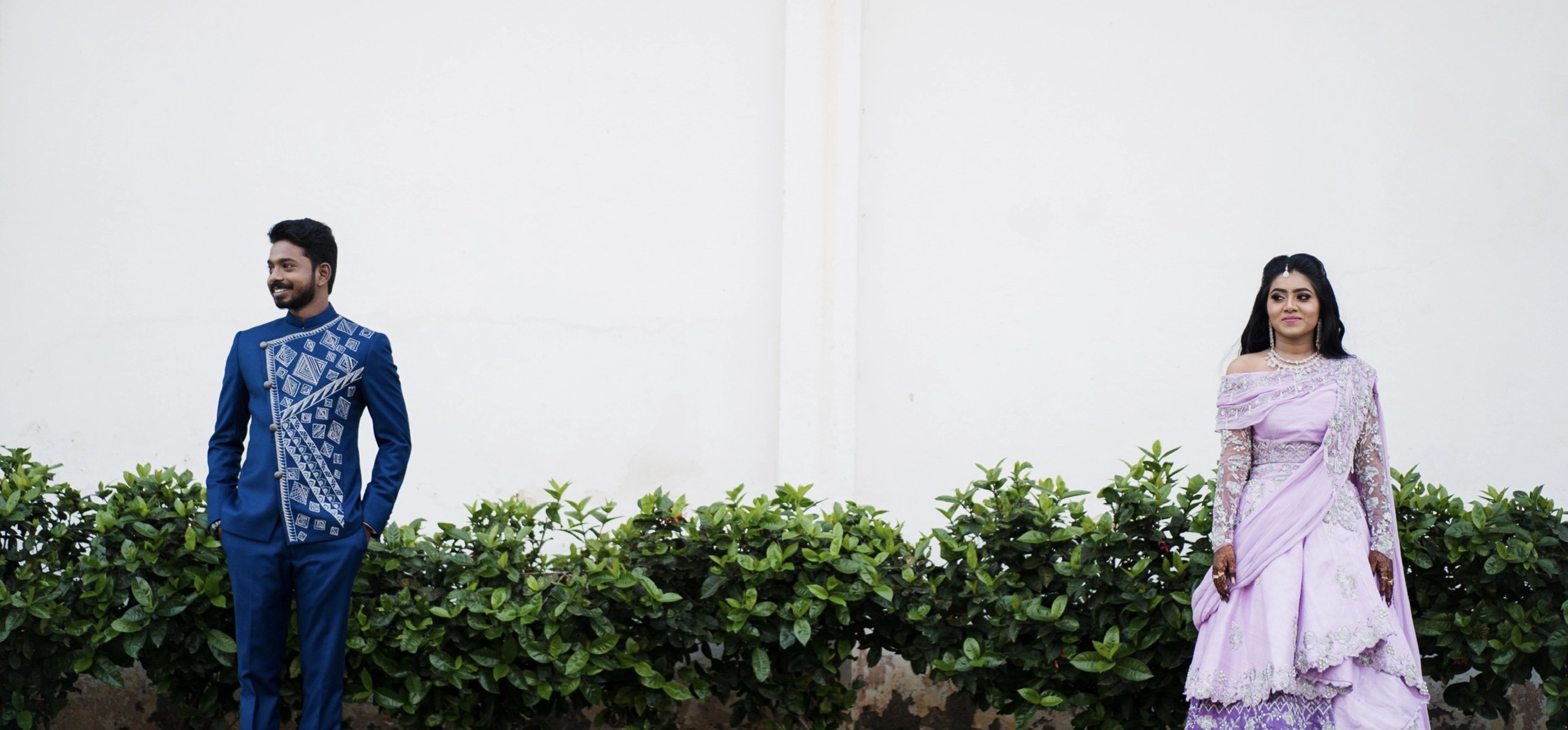 Couple posing for photo in a lilac raw silk lehenga and blue indo-western bandhgala handcrafted by team Archana Karthick.