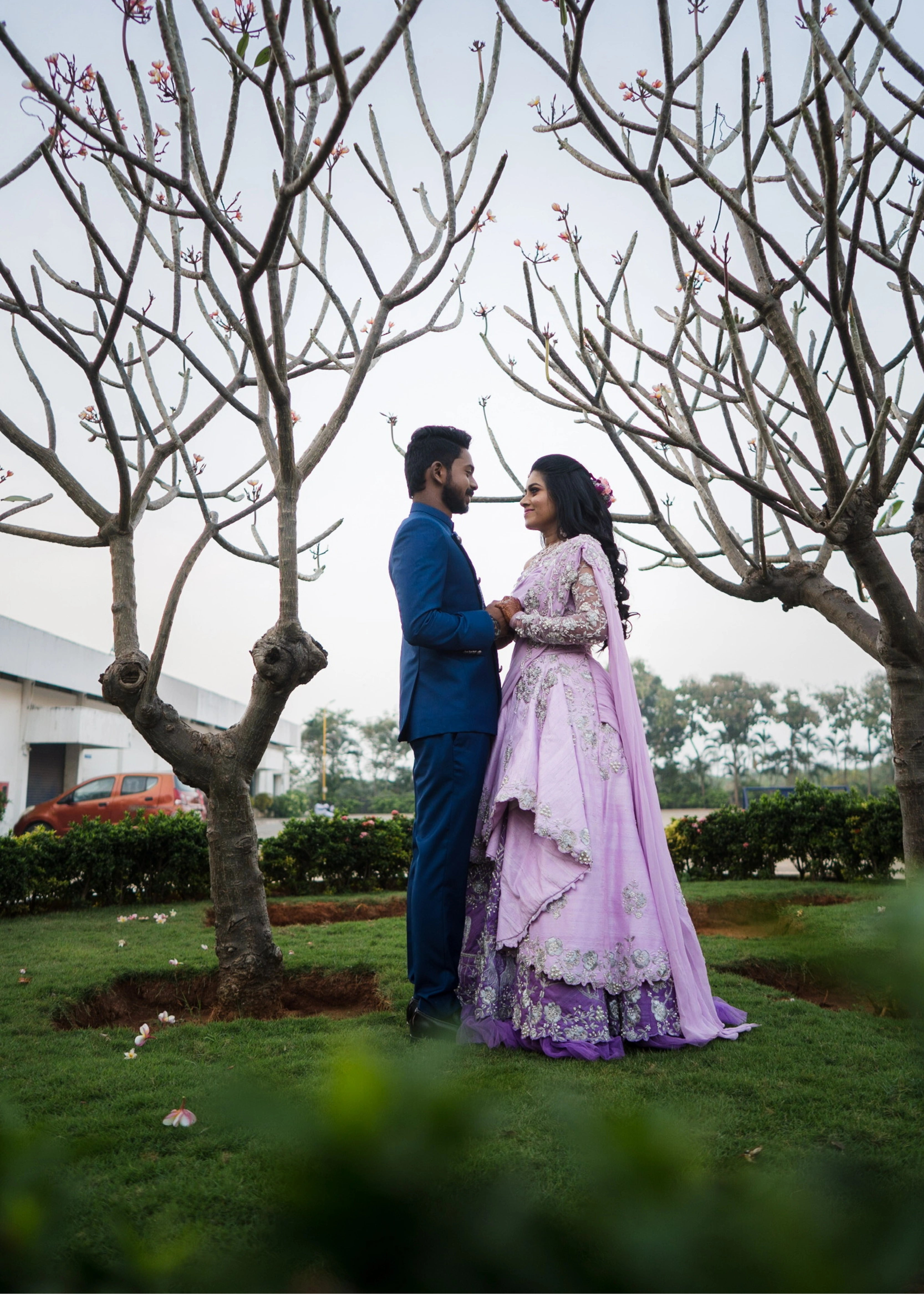 Couple posing in a lilac raw silk lehenga and blue indo-western bandhgala handcrafted by team Archana Karthick.