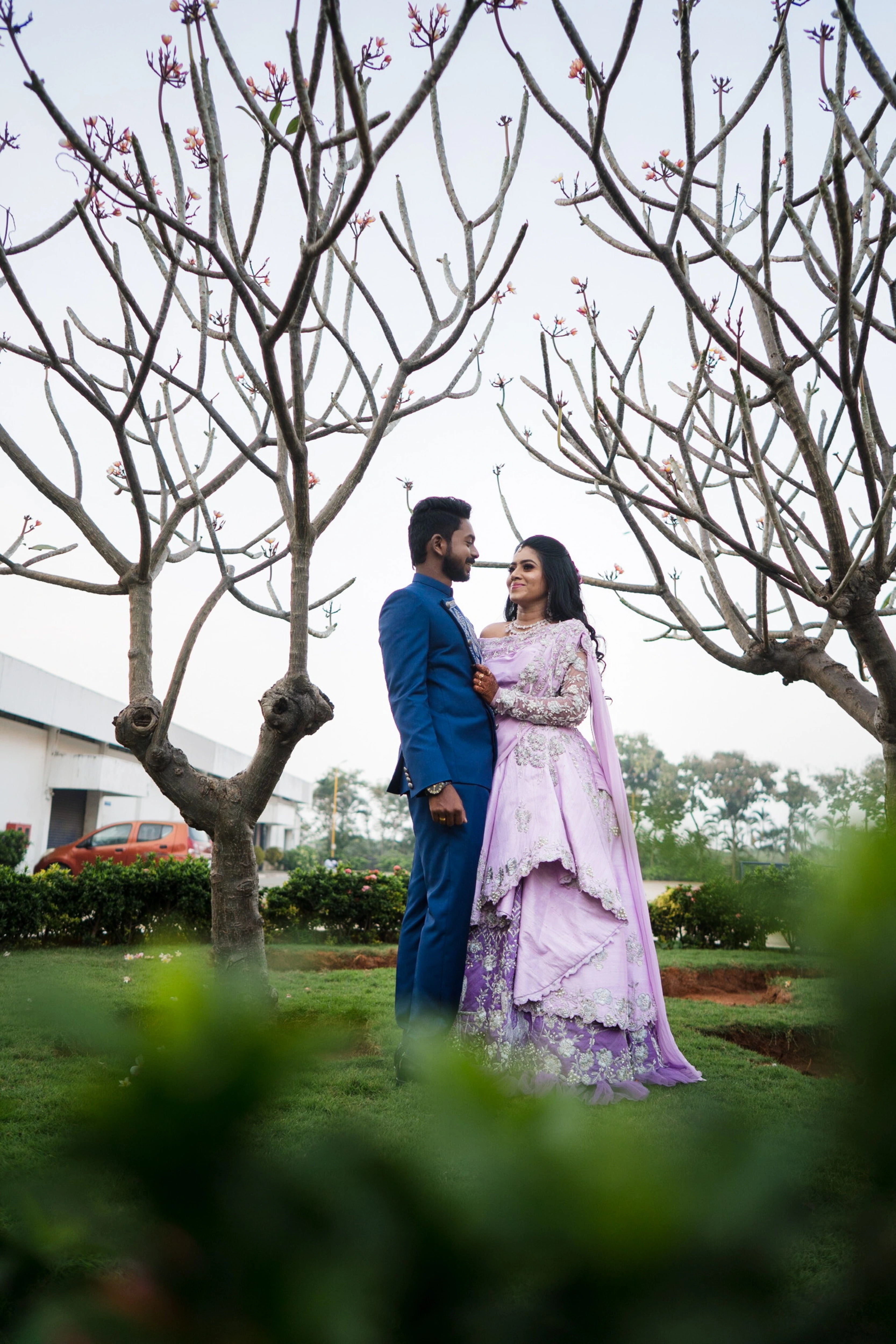 Couple smiling in a lilac raw silk lehenga and blue indo-western bandhgala handcrafted by team Archana Karthick.