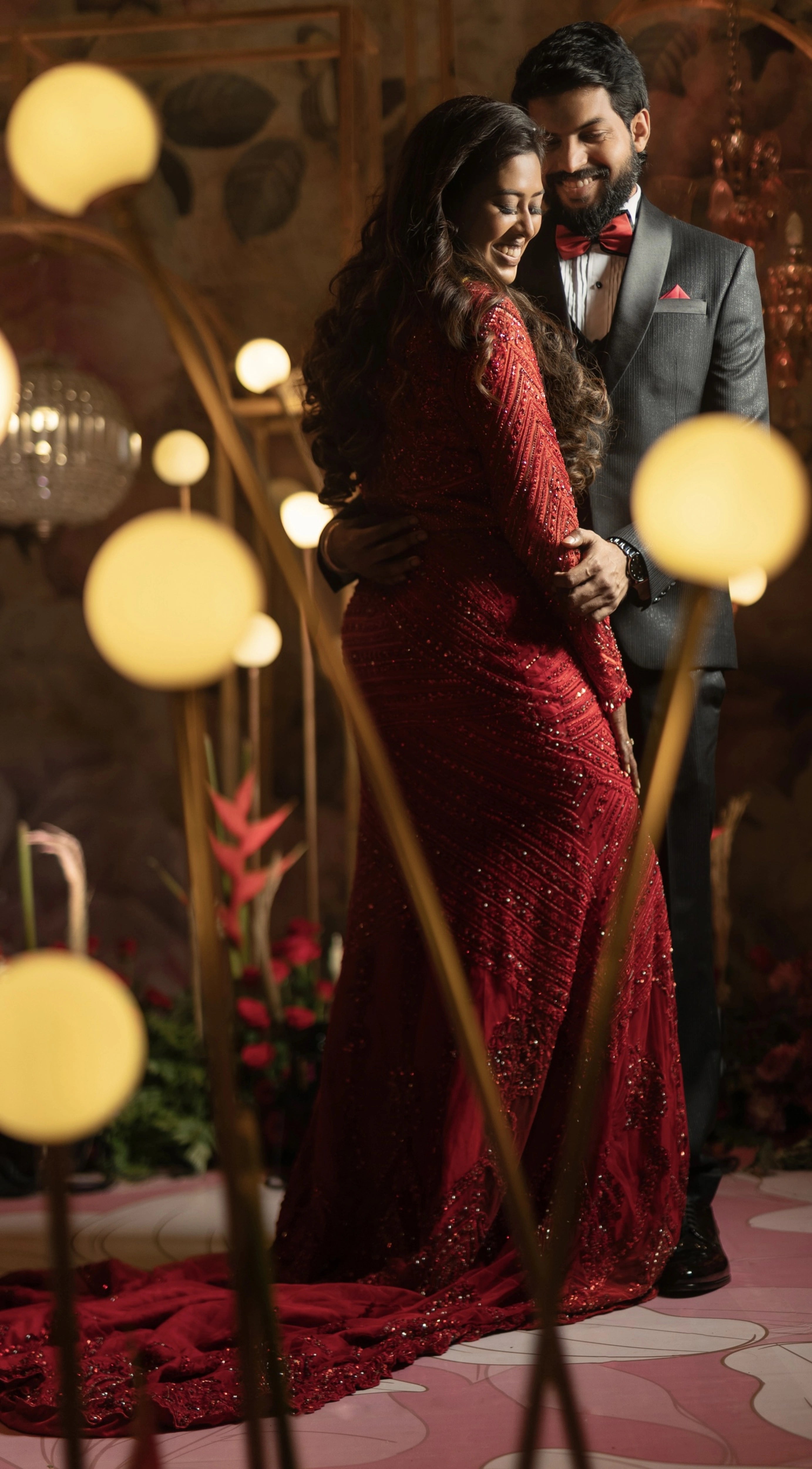 Dr Vishu Priya smiling with groom in a ruby red mermaid gown intricately handcrafted by team Archana Karthick.