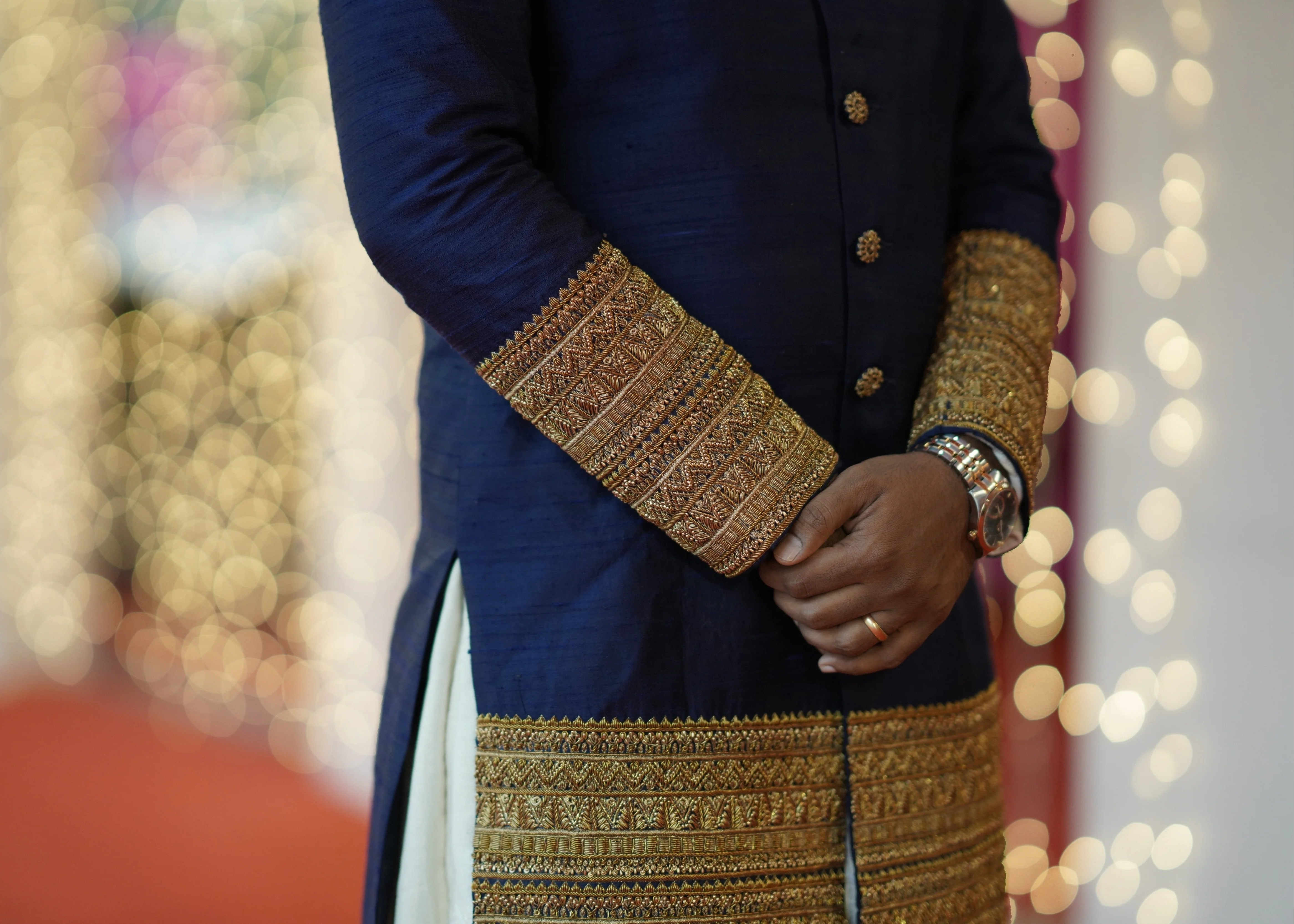Groom Dinesh from Dindigul in a navy blue raw silk sherwani with embellished cuffs, collar and borders designed by Archana Karthick for his reception in a closeup of cuffs and borders