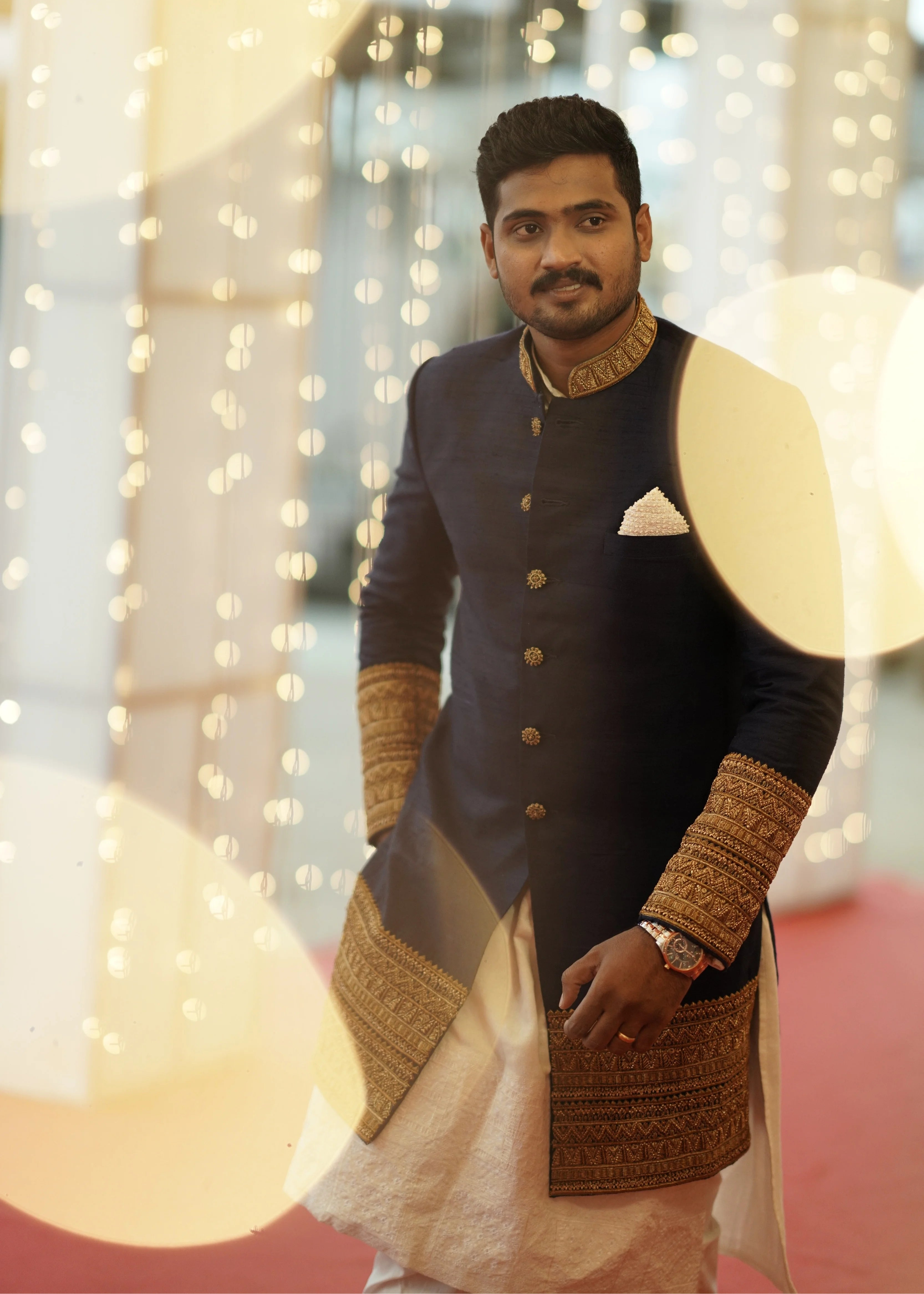 Groom Dinesh from Dindigul in a navy blue raw silk sherwani with embellished cuffs, collar and borders designed by Archana Karthick for his reception posing for a portrait