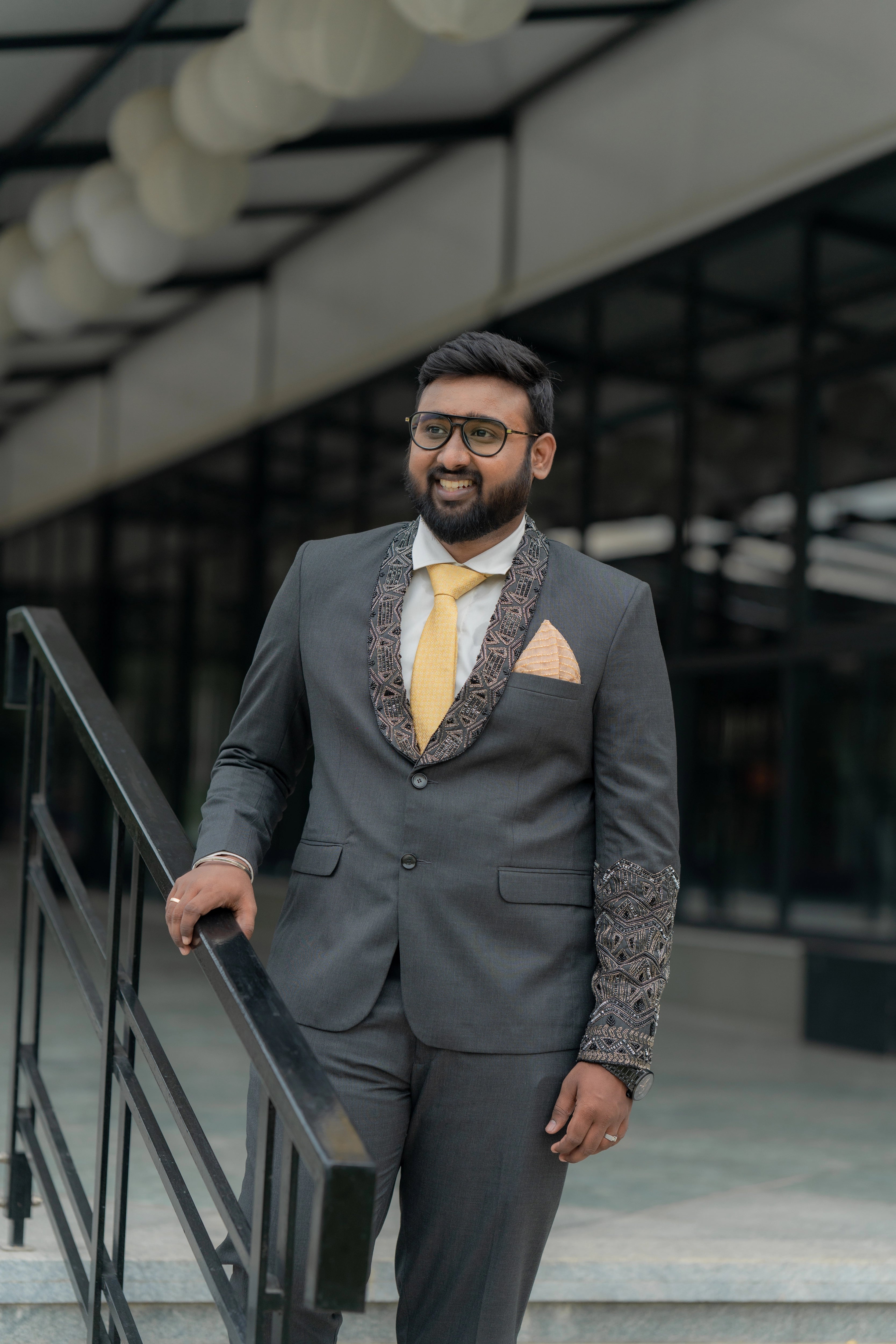 Groom Jai posing in a bespoke charcoal grey suit, with lapels intricately handcrafted with beads and sequins by team Archana Karthick.