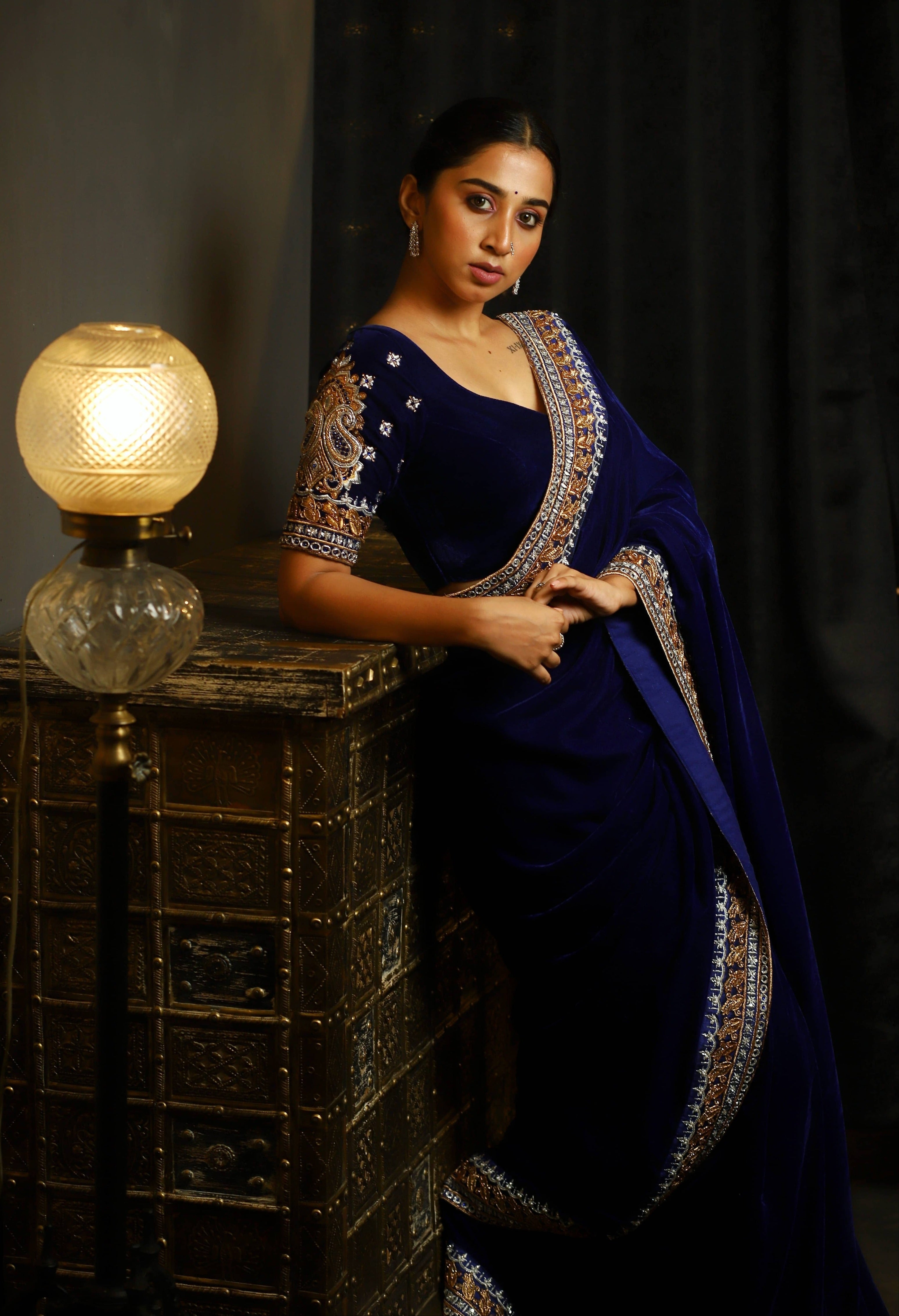 Influencer Deekshita Nikkam in a navy velvet saree and blouse set with zardozi detailings on border and sleeves. Side profile leaning on a chest