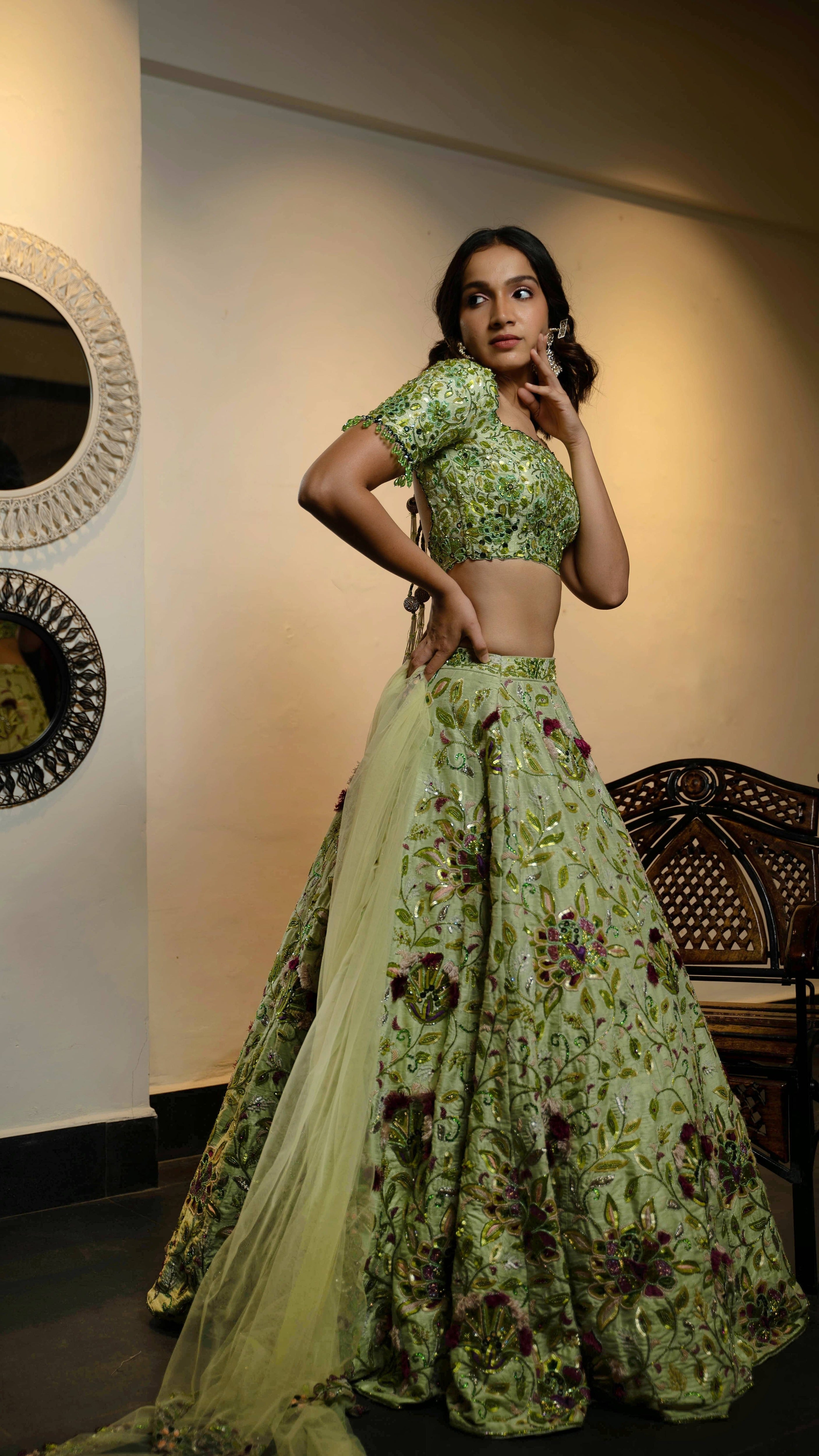 Influencer and actress Shweta Gai in a handcrafted green raw silk lehenga with floral motifs by Archana Karthick. Posing with dupatta in her right hand and looking to her right with one hand on cheek.