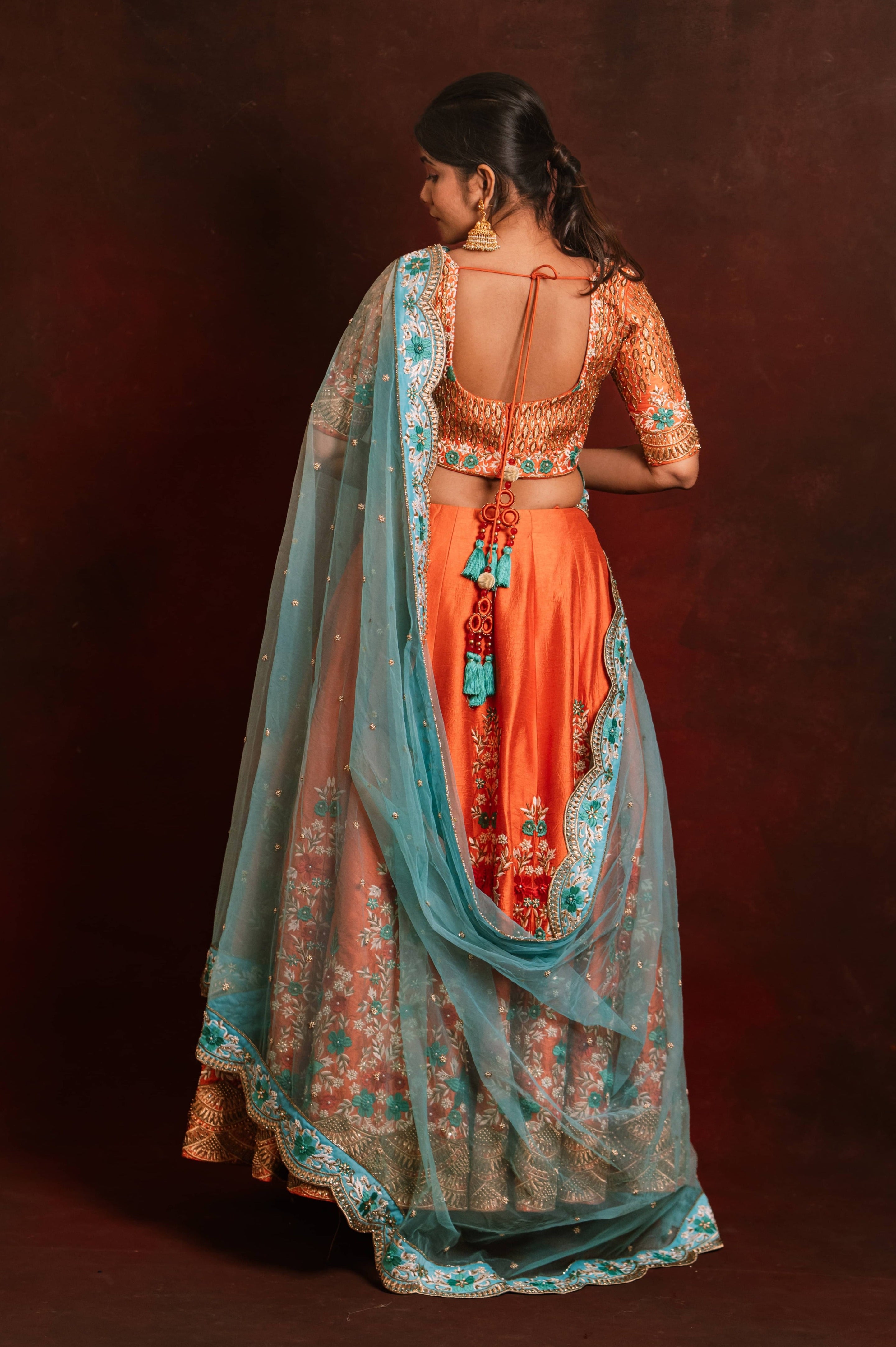 Jaina Parmar, known for recreating looks of actress Nayanthara is seen here posing in a raw silk burnt orange lehenga with blue net dupatta. Full back design