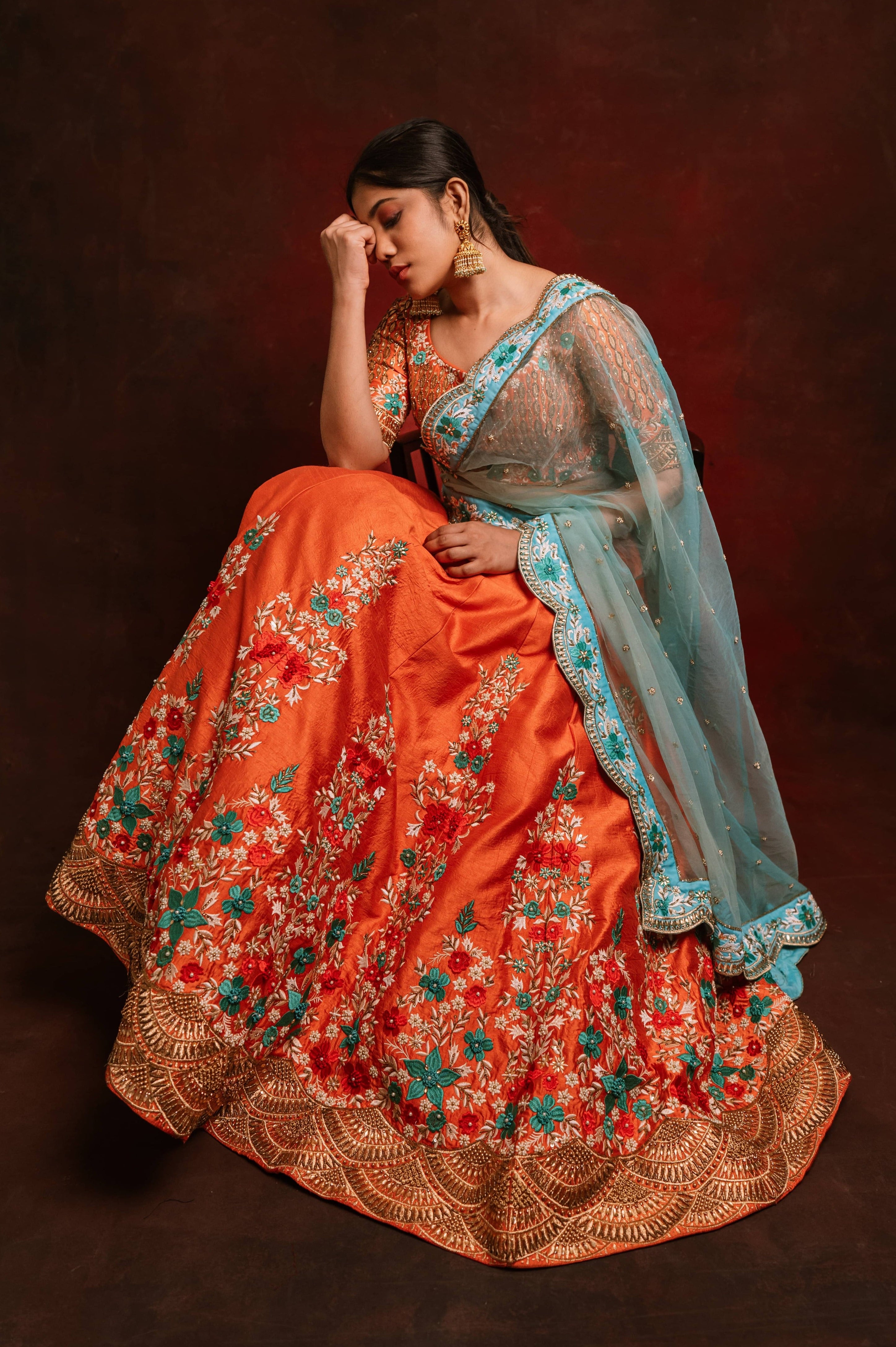 Jaina Parmar, known for recreating looks of actress Nayanthara is seen here posing in a raw silk burnt orange lehenga with blue net dupatta. Full seated pose