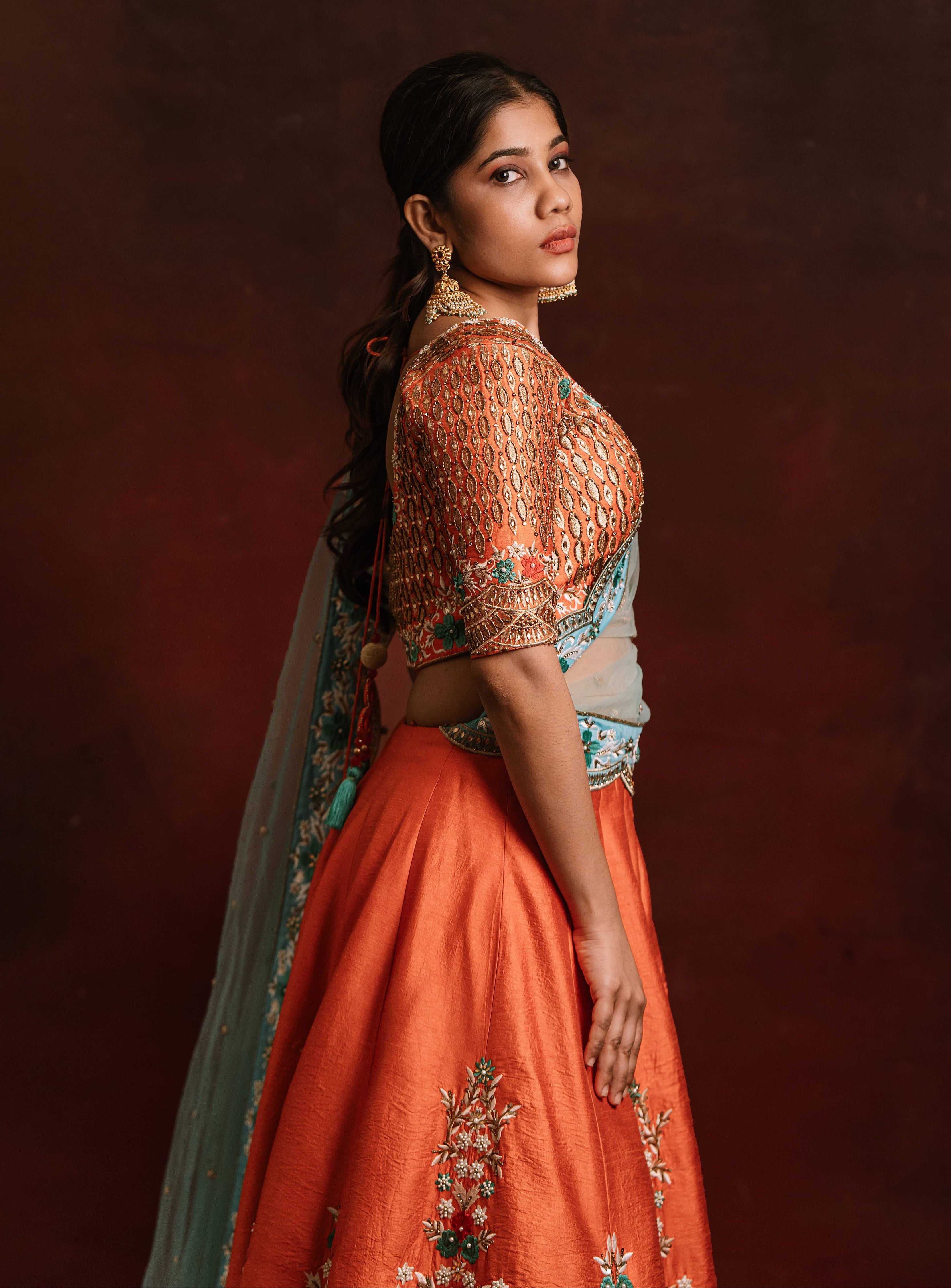 Jaina Parmar, known for recreating looks of actress Nayanthara is seen here posing in a raw silk burnt orange lehenga with blue net dupatta. Full sleeve design