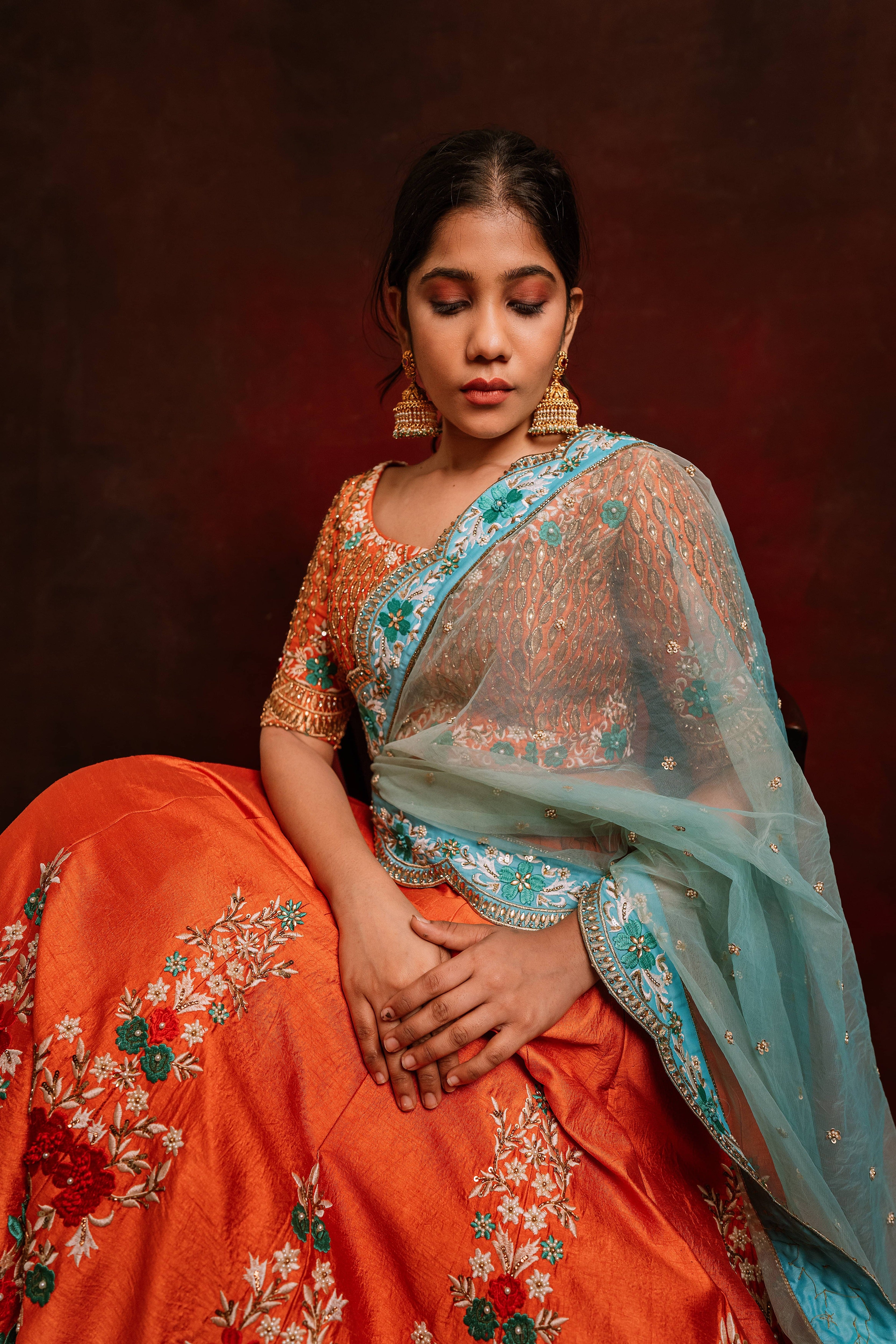 Jaina Parmar, known for recreating looks of actress Nayanthara is seen here posing in a raw silk burnt orange lehenga with blue net dupatta. seated pose