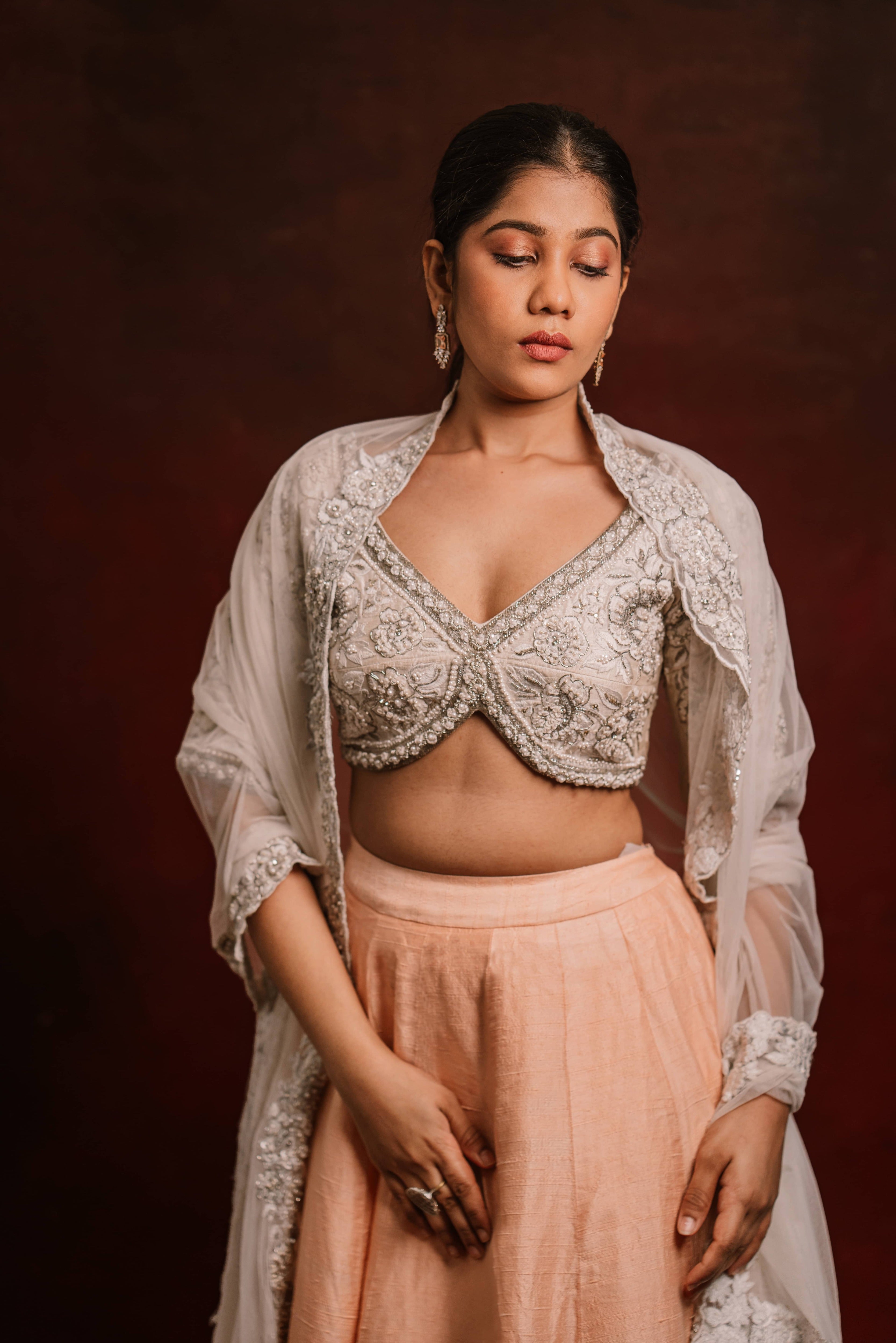 Jaina Parmar, known for recreating looks of actress Nayanthara is seen here posing in an ivory and peach raw silk lehenga with net dupatta. It has pearl and zari embellishments.