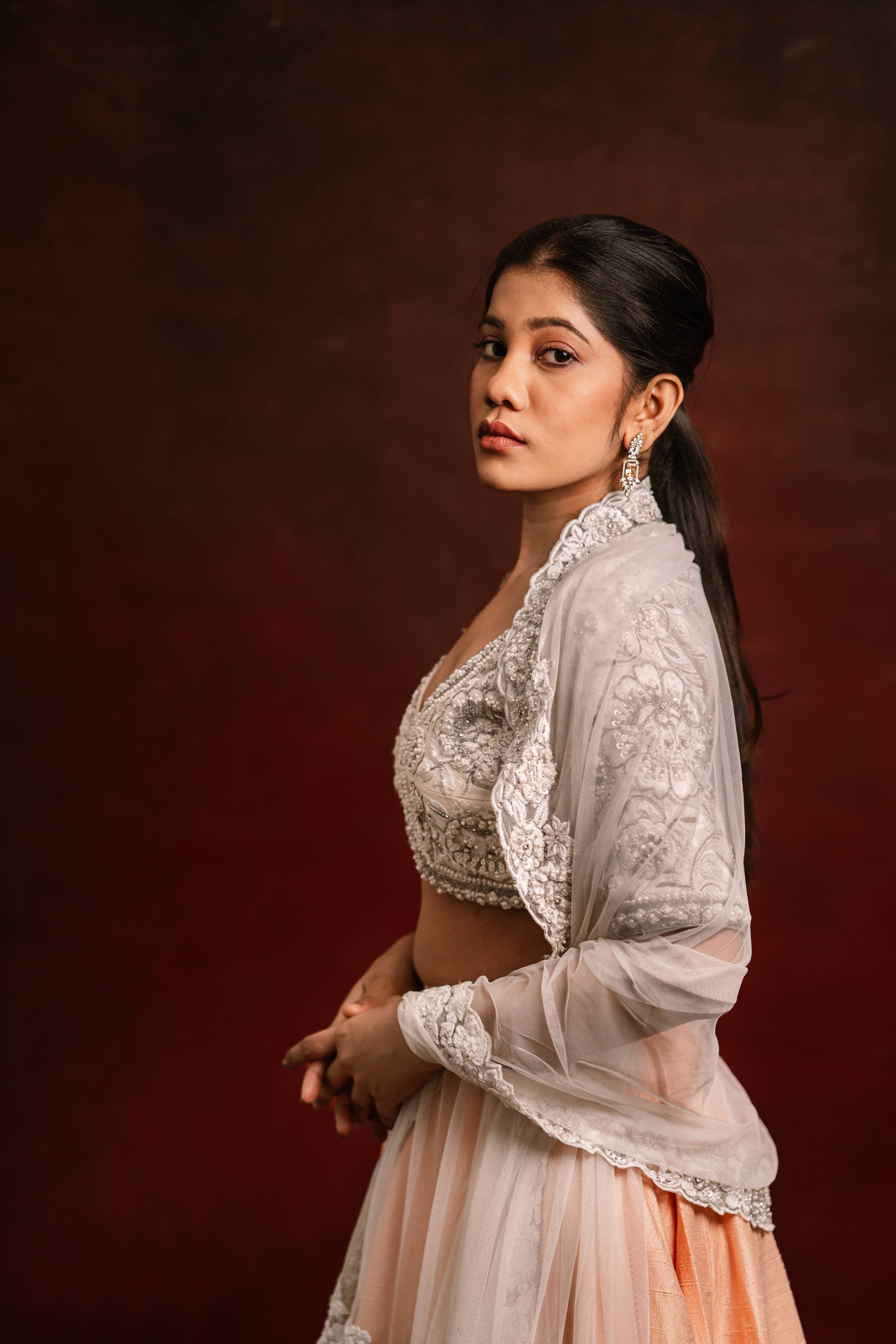 Jaina Parmar, known for recreating looks of actress Nayanthara is seen here posing in an ivory and peach raw silk lehenga with net dupatta. Side profile captured.