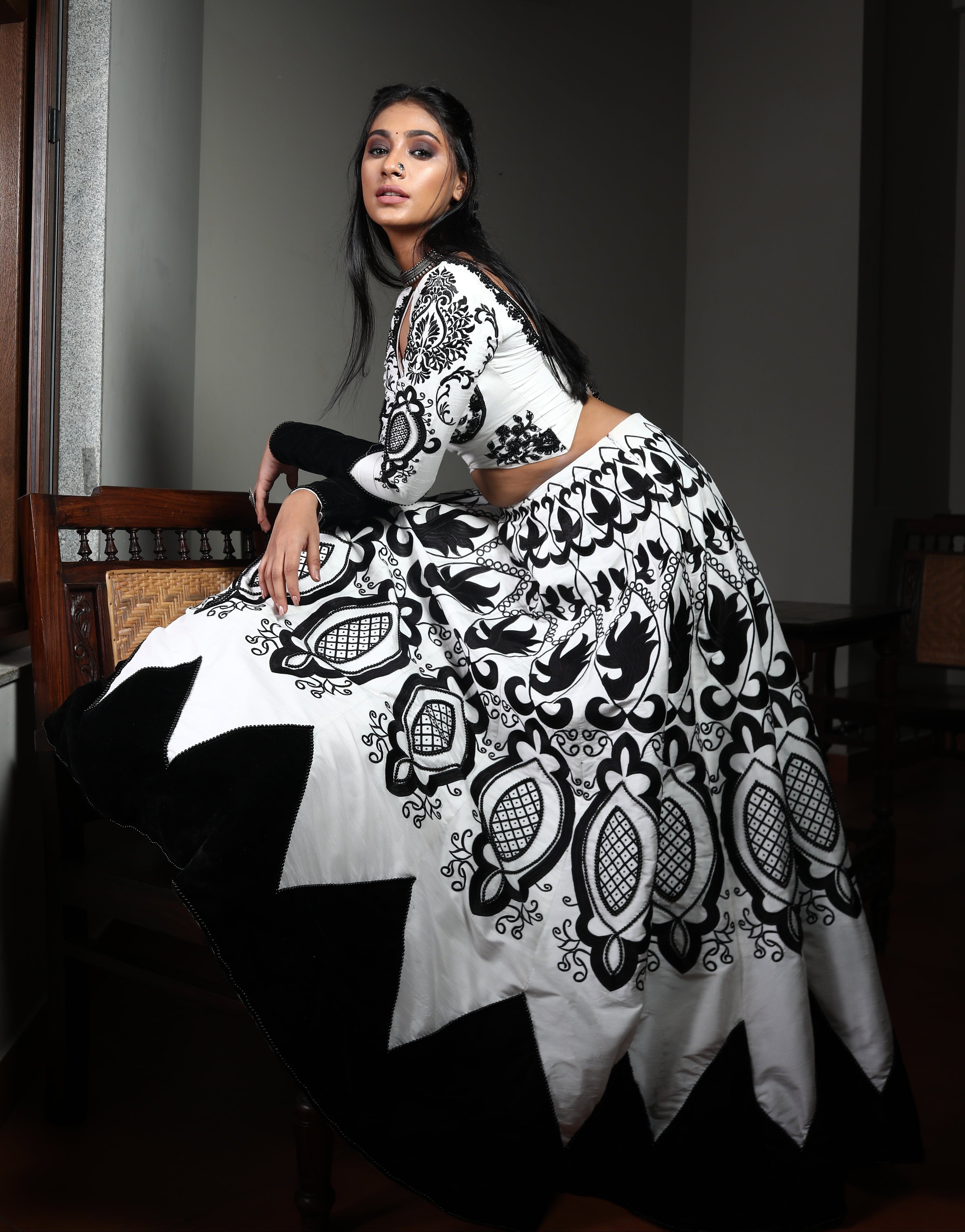 Miss India 2018 Anukreethy Vas in white raw sIlk lehenga with motifs in black velvet posing sideways with one leg on the antique sofa with a sultry look at the lens. This lehenga is designed by Archana Karthick