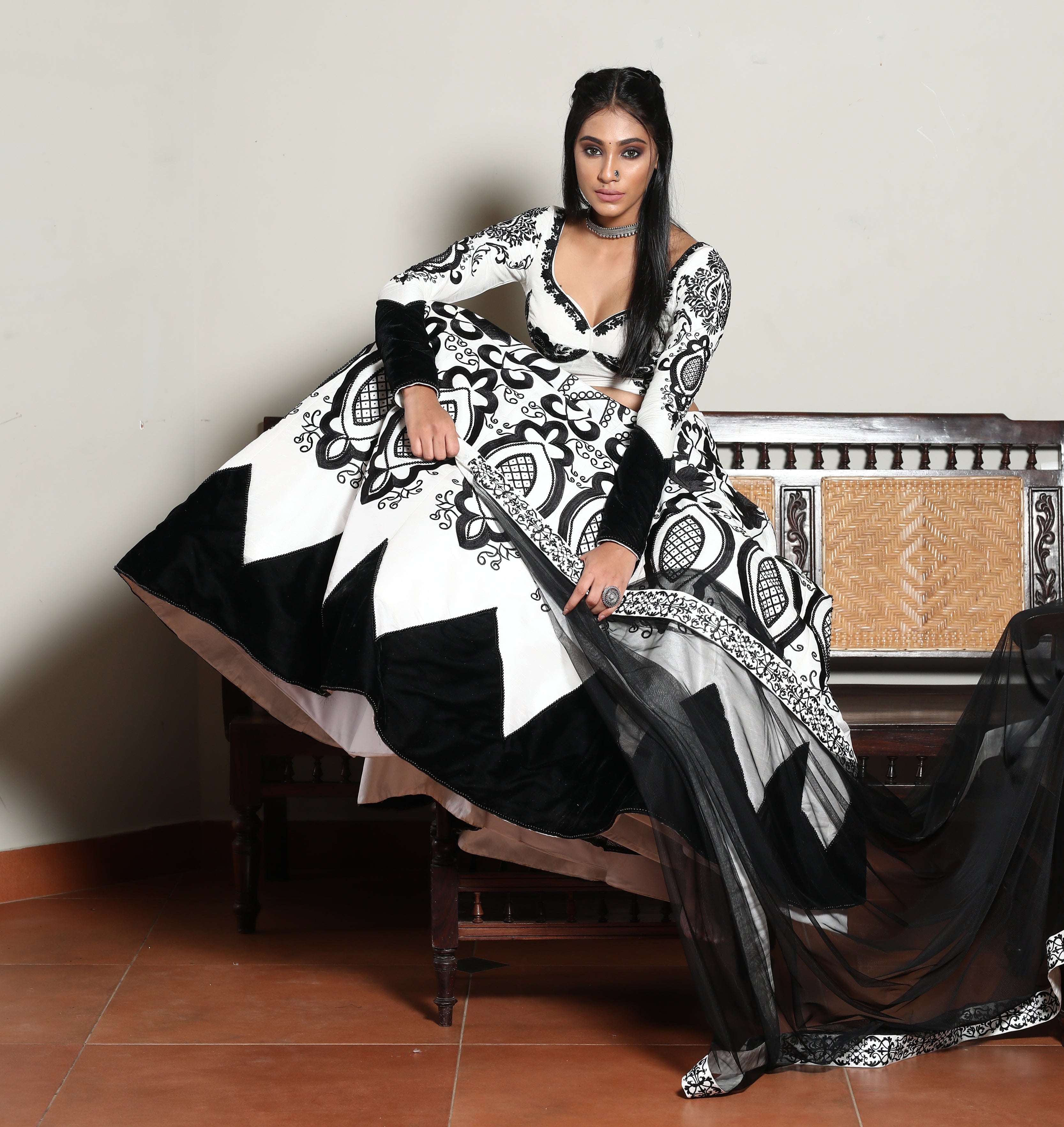 Miss India 2018 Anukreethy Vas in white raw sIlk lehenga with motifs in black velvet posing sitting on the arm rest of an antique sofa with a straight look at the lens. This lehenga is designed by Archana Karthick