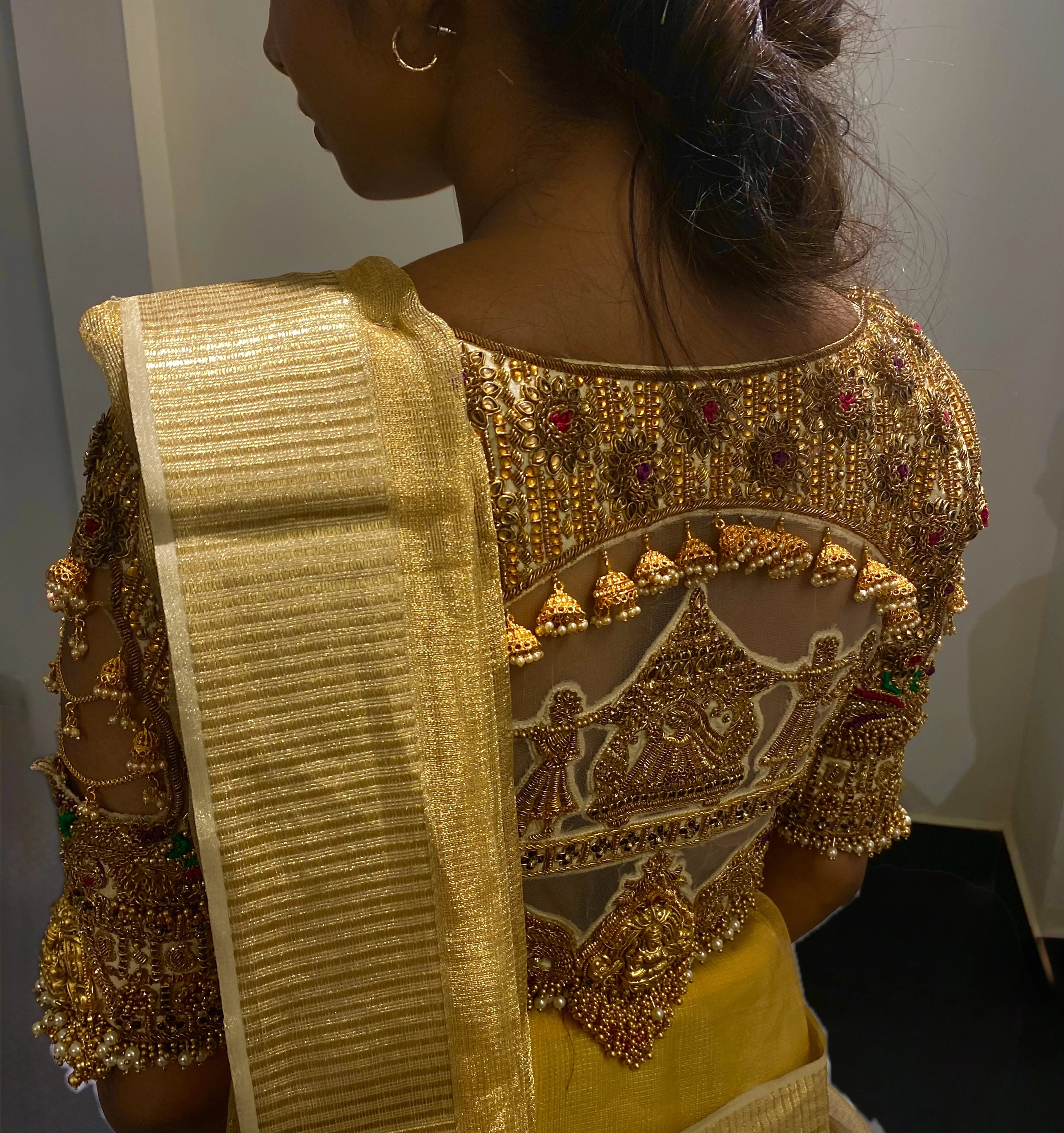 Model Aaveline Ramesh showcasing the back blouse detailings in a gold silk blouse with intricate kemp stones and jhumki embellishments designed by team Archana Karthick.