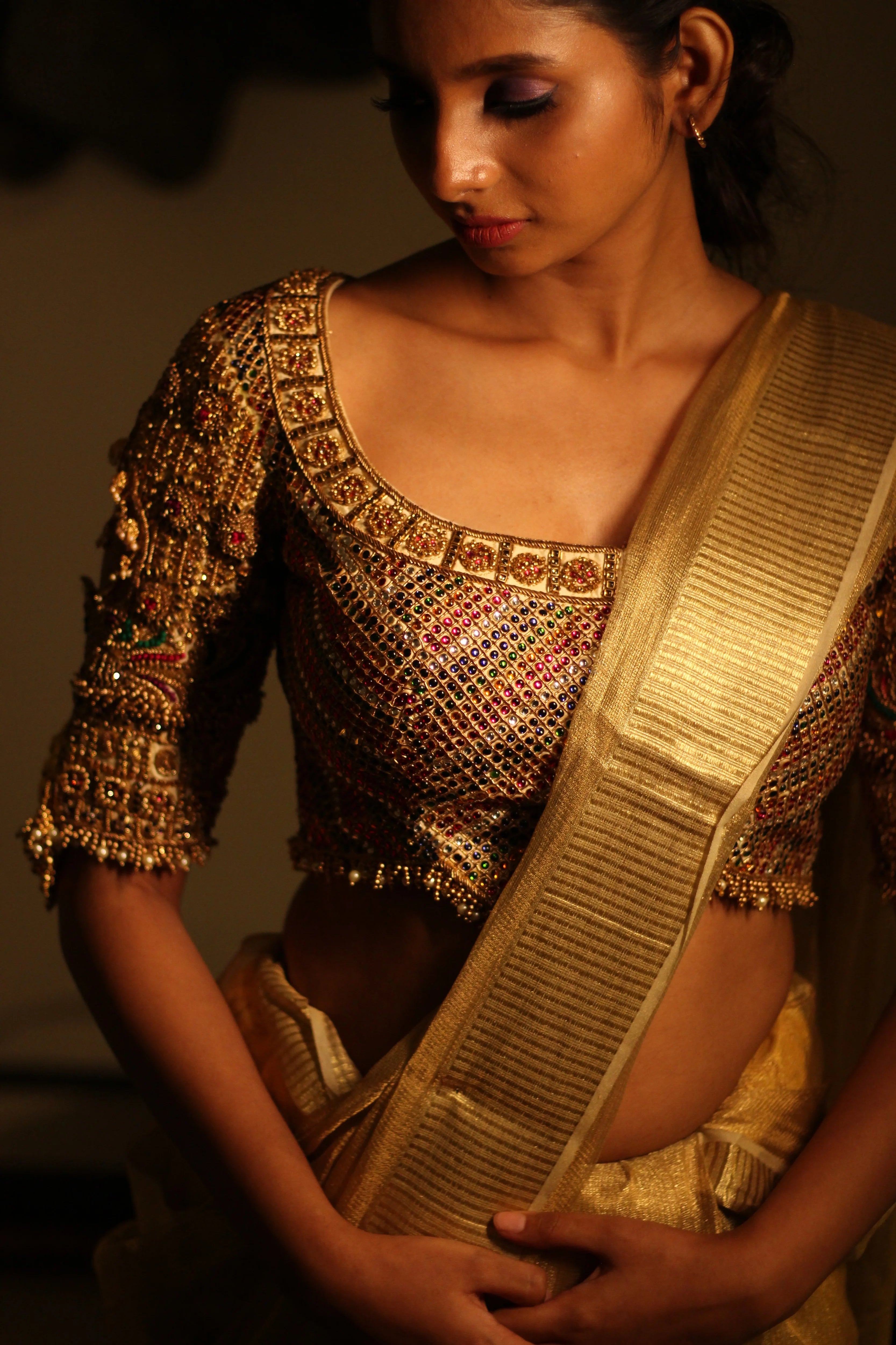 Model Aaveline Ramesh showcasing the blouse detailings in a gold silk blouse with intricate kemp stones and jhumki embellishments designed by team Archana Karthick.
