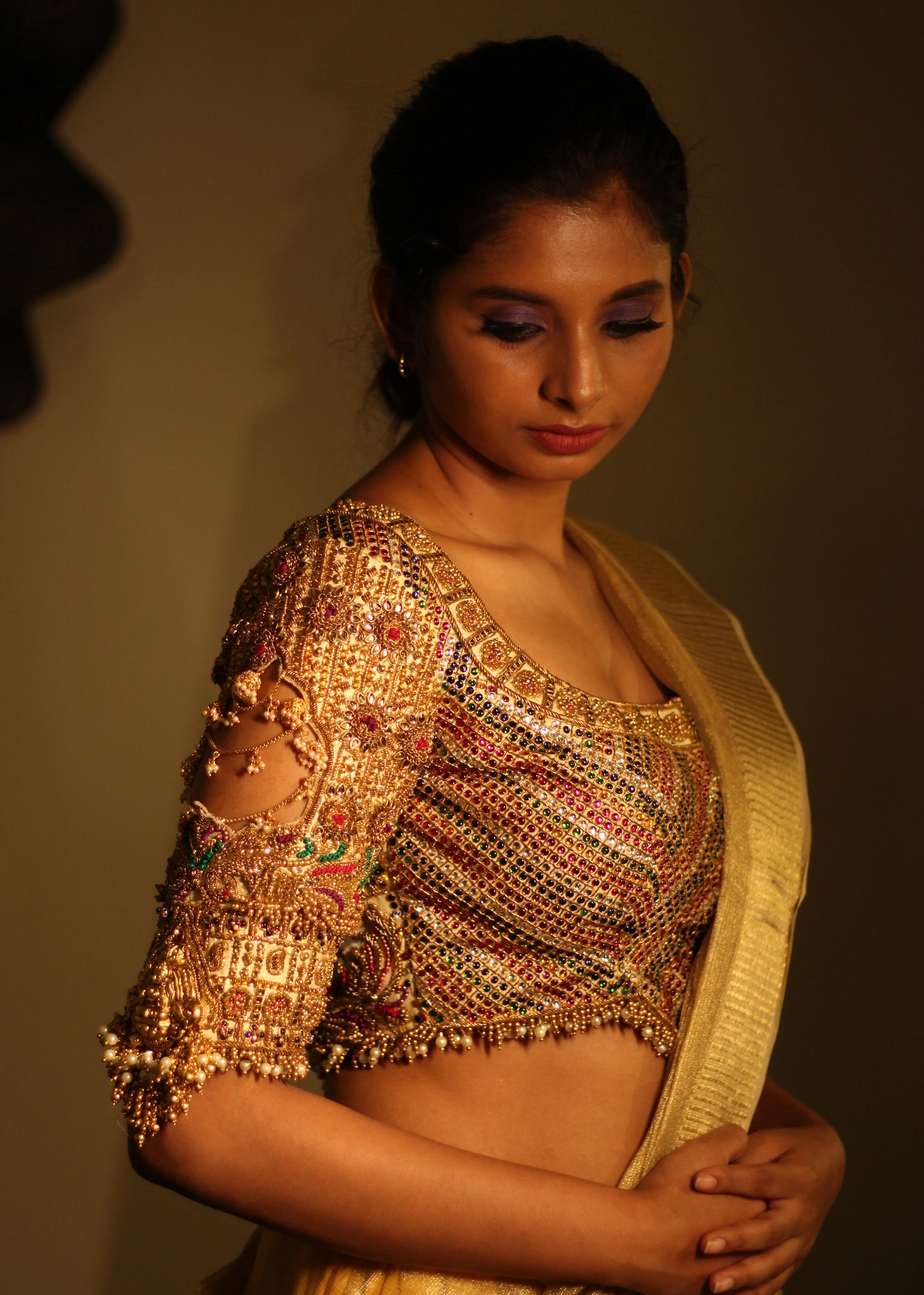 Model Aaveline Ramesh showcasing the sleeve detailings in a gold silk blouse with intricate kemp stones and jhumki embellishments designed by team Archana Karthick.