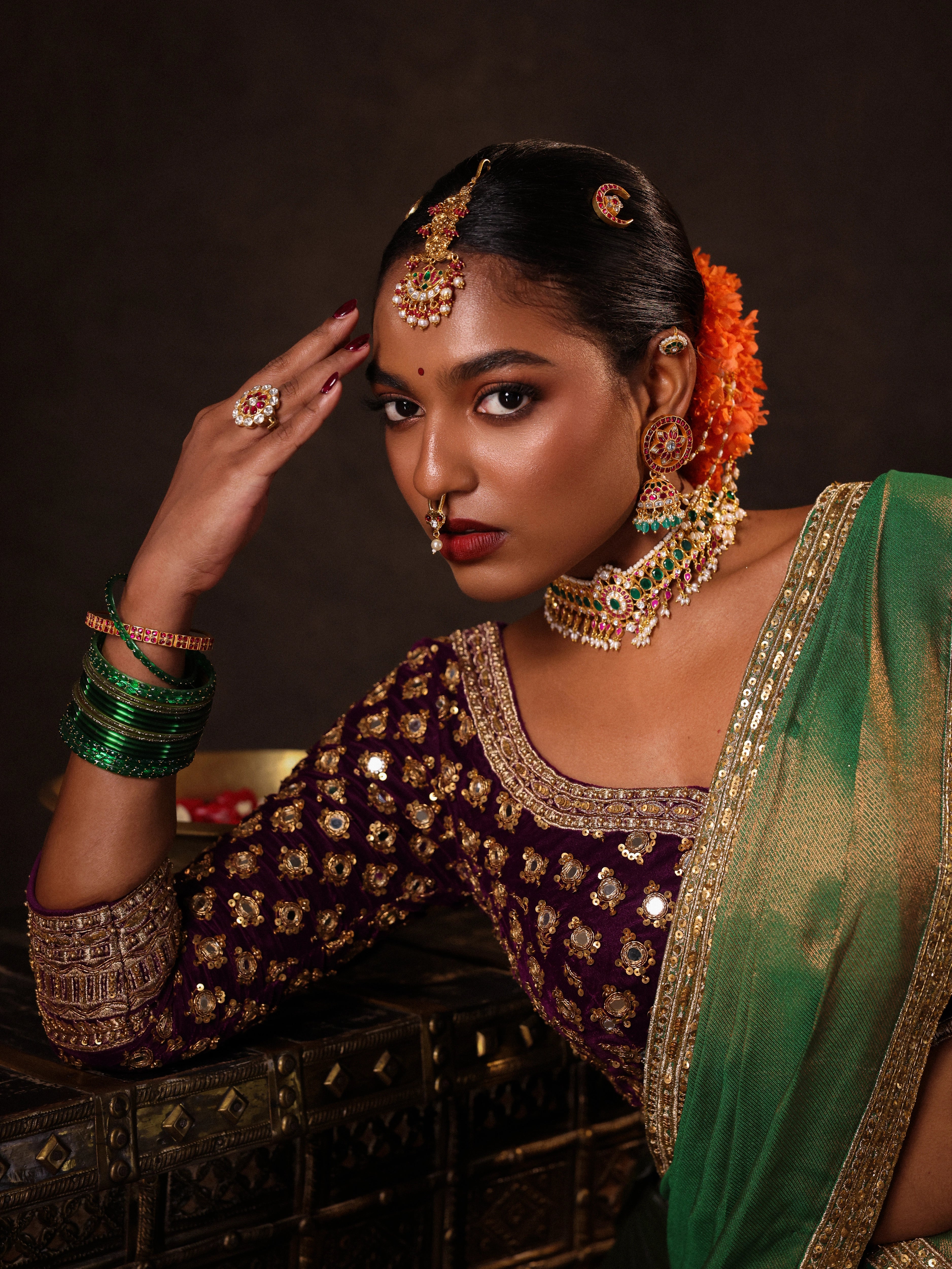 Model Ashika Crystal for a closeup shot in a green and purple half saree set with a velvet blouse, tissue silk dupatta and brocade skirt handcrafted with zardozi, mirror, zari, cutdana and sequins. Team Archana Karthick completed the style with green glass bangles, a ring, a choker, jhumkas, nose ring and a maang tikka.