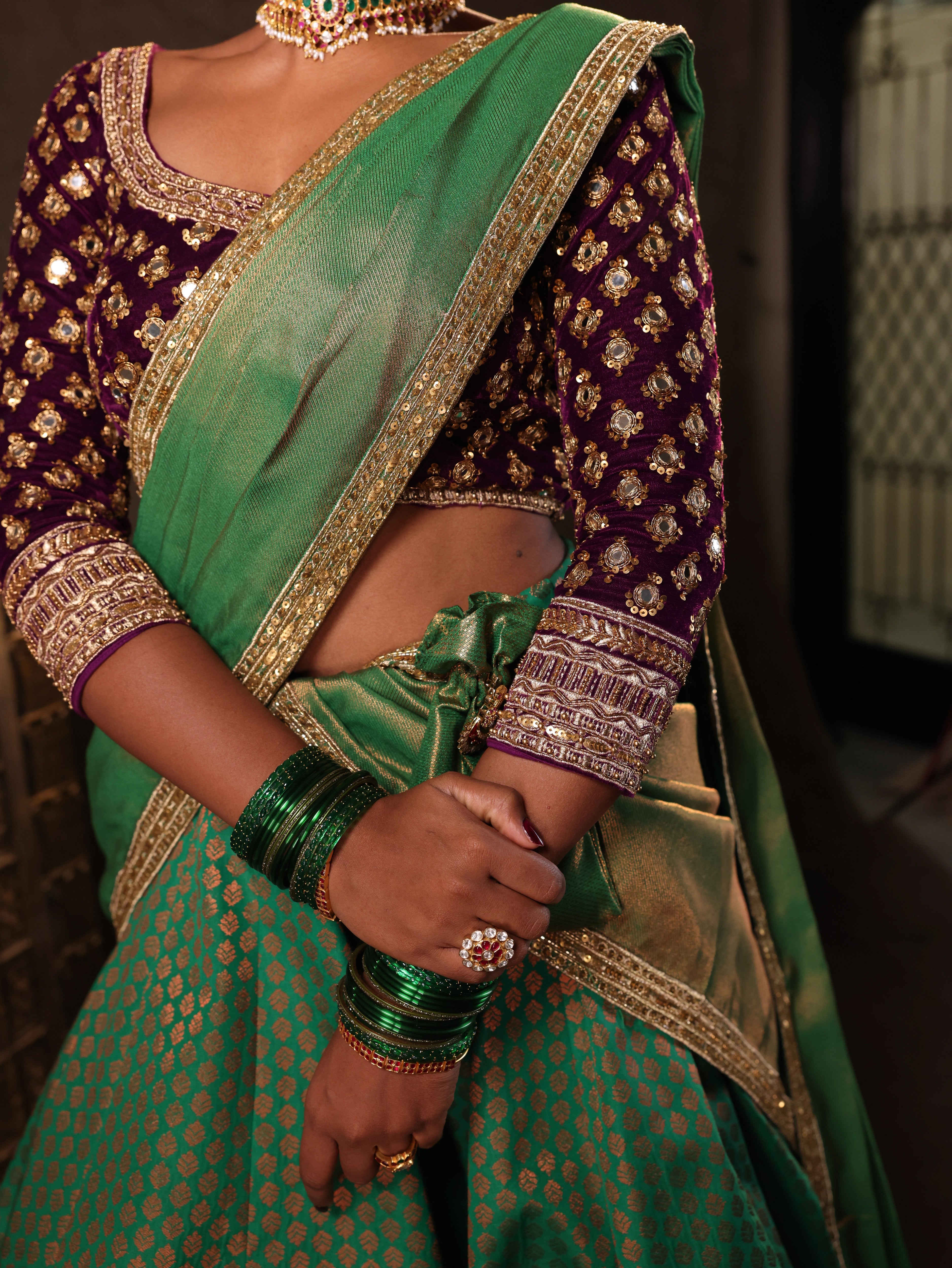 Model Ashika Crystal for a detailing shot in a green and purple half saree set with a velvet blouse, tissue silk dupatta and brocade skirt handcrafted with zardozi, mirror, zari, cutdana and sequins. Team Archana Karthick completed the style with green glass bangles, a ring, a choker, jhumkas, nose ring and a maang tikka.