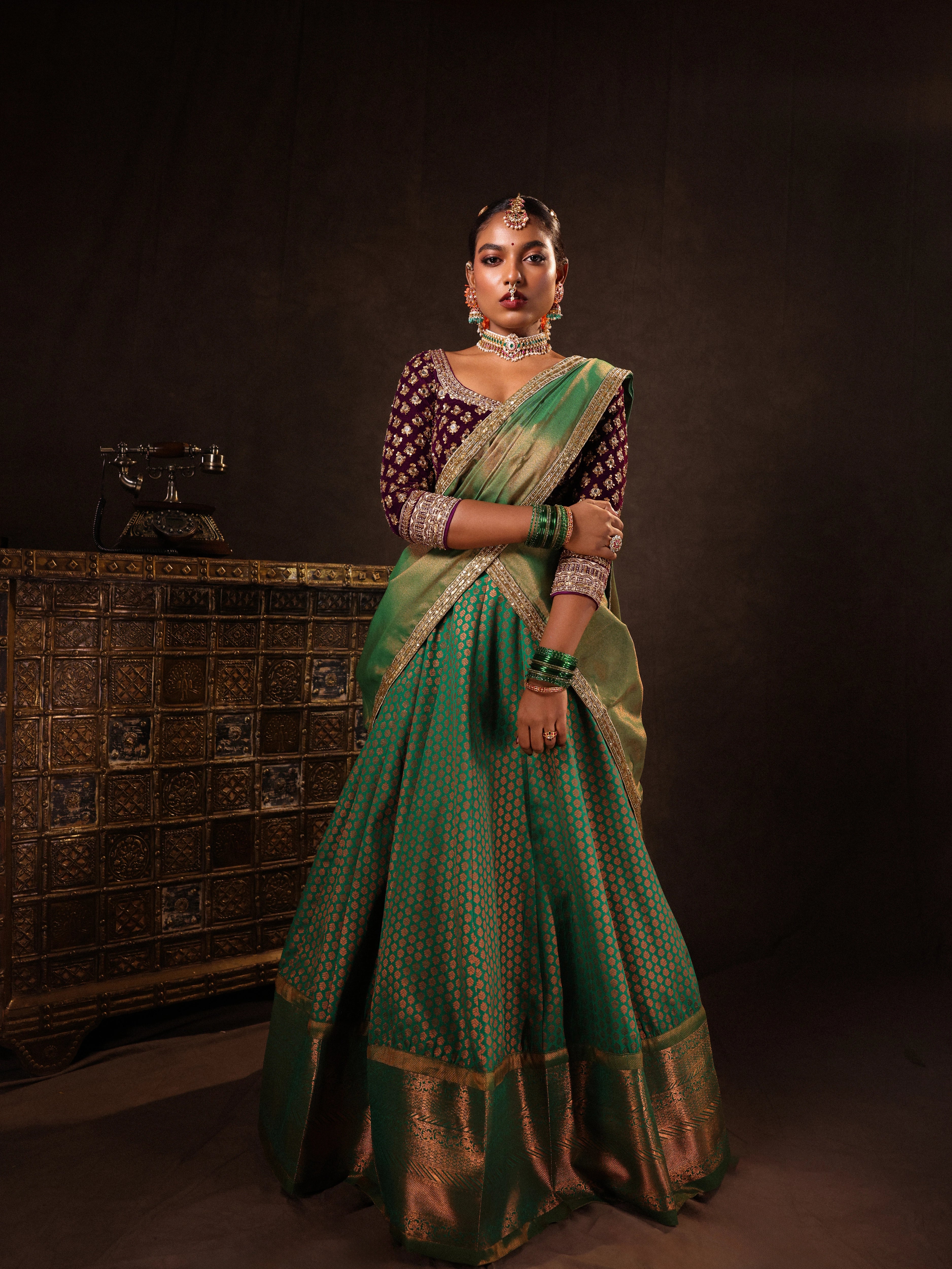 Model Ashika Crystal in a green and purple half saree set with a velvet blouse, tissue silk dupatta and brocade skirt handcrafted with zardozi, mirror, zari, cutdana and sequins. Team Archana Karthick completed the style with green glass bangles, a ring, a choker, jhumkas, nose ring and a maang tikka.