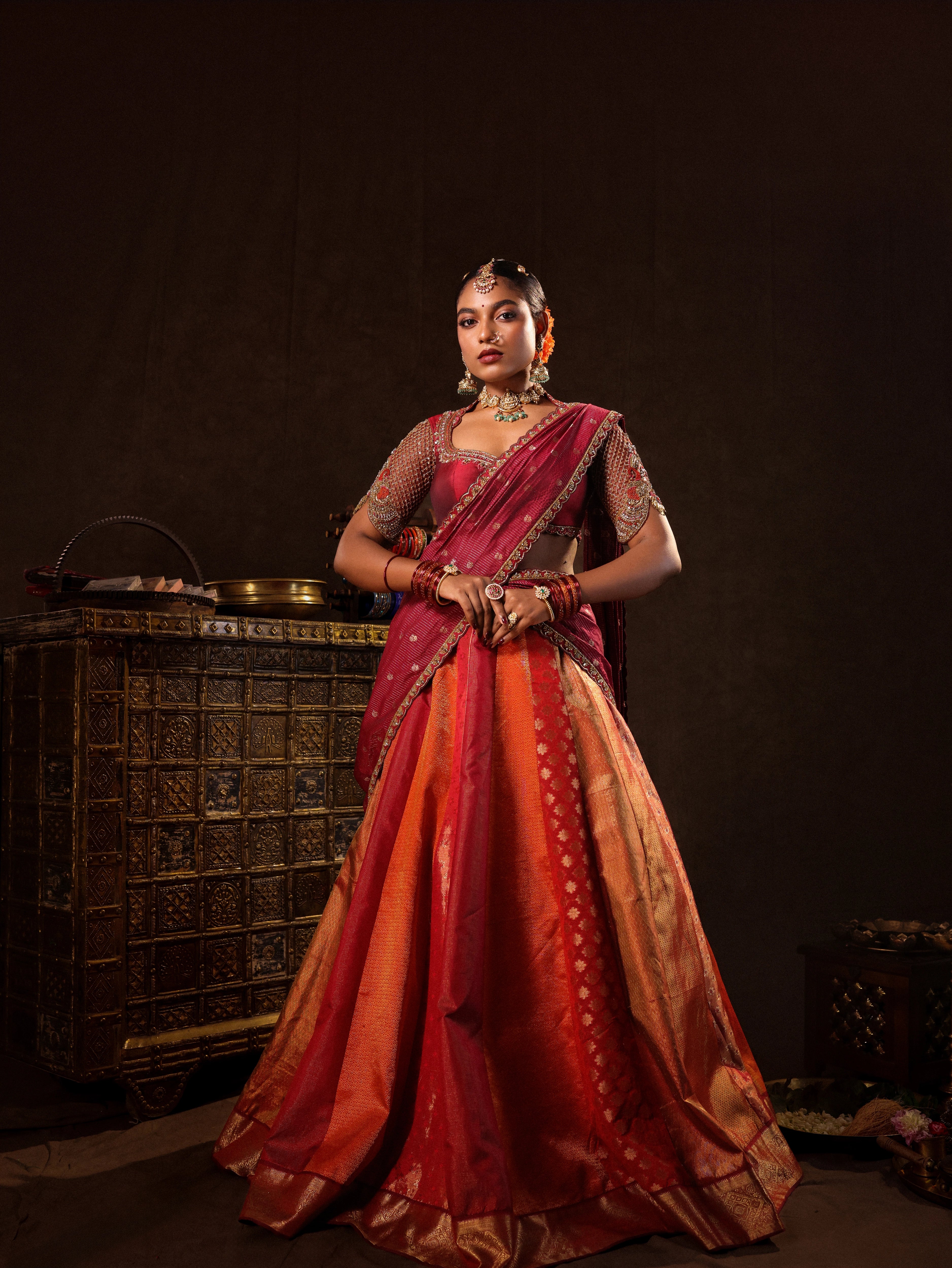 Model Ashika Crystal in a red and orange silk half saree with a scalloped veil is handrcrafted with sequins, cutdana, resham, stones and exquisite hangings by team Archana Karthick