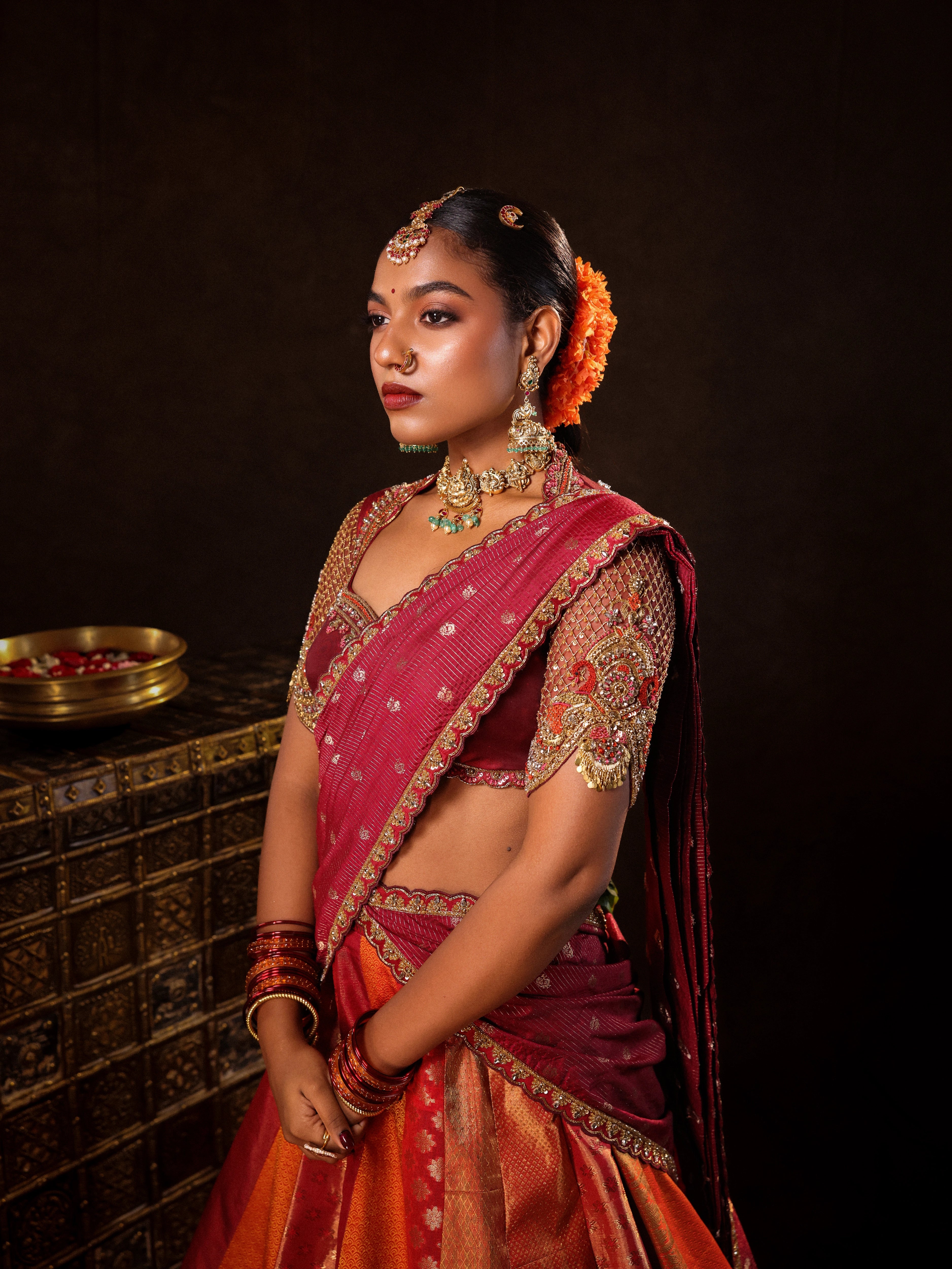 Model Ashika Crystal posing during photoshoot in a red and orange silk half saree with a scalloped veil is handrcrafted with sequins, cutdana, resham, stones and exquisite hangings. Team Archana Karthick completed the style with orange & red glass bangles, a ring, jhumkas, nose ring and a maang tikka.