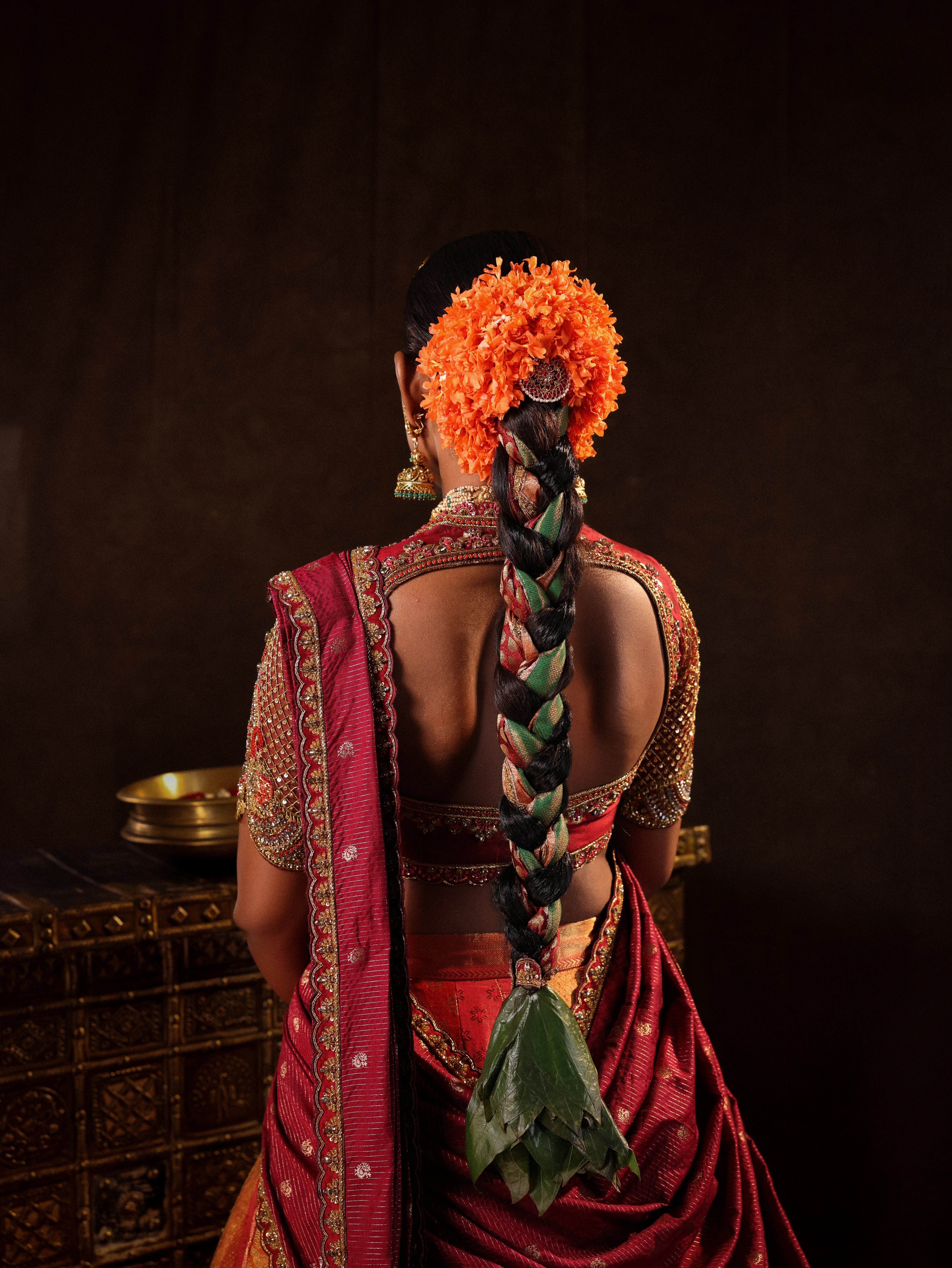 Model Ashika Crystal posing for blouse back and braid detailing in a red and orange silk half saree with a scalloped veil is handrcrafted with sequins, cutdana, resham, stones and exquisite hangings. Team Archana Karthick completed the style with orange & red glass bangles, a ring, jhumkas, nose ring and a maang tikka.