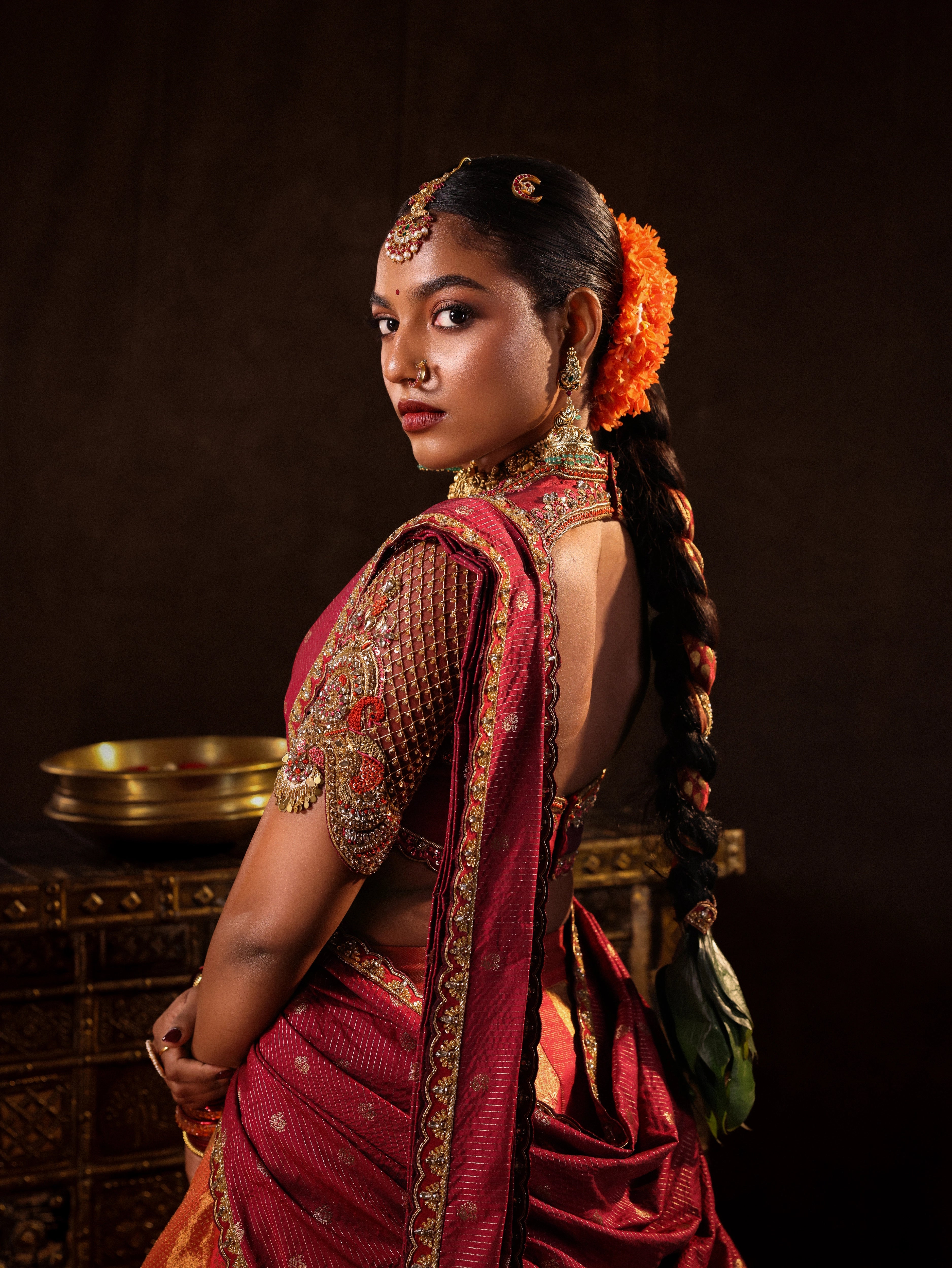 Model Ashika Crystal posing for blouse back and sleeve detailing in a red and orange silk half saree with a scalloped veil is handrcrafted with sequins, cutdana, resham, stones and exquisite hangings. Team Archana Karthick completed the style with orange & red glass bangles, a ring, jhumkas, nose ring and a maang tikka.