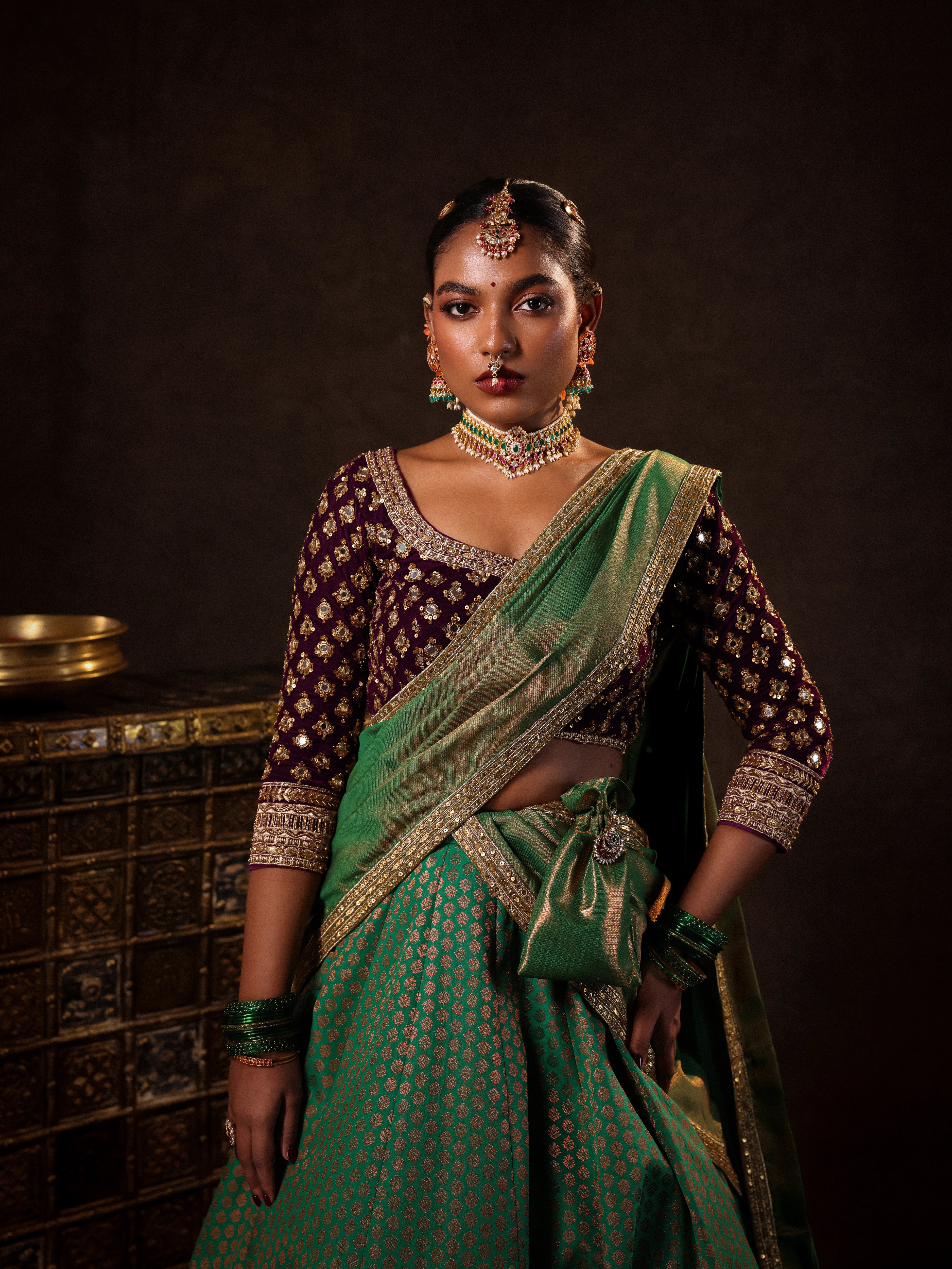 Model Ashika Crystal posing for front detailing in a green and purple half saree set with a velvet blouse, tissue silk dupatta and brocade skirt handcrafted with zardozi, mirror, zari, cutdana and sequins. Team Archana Karthick completed the style with green glass bangles, a ring, a choker, jhumkas, nose ring and a maang tikka.
