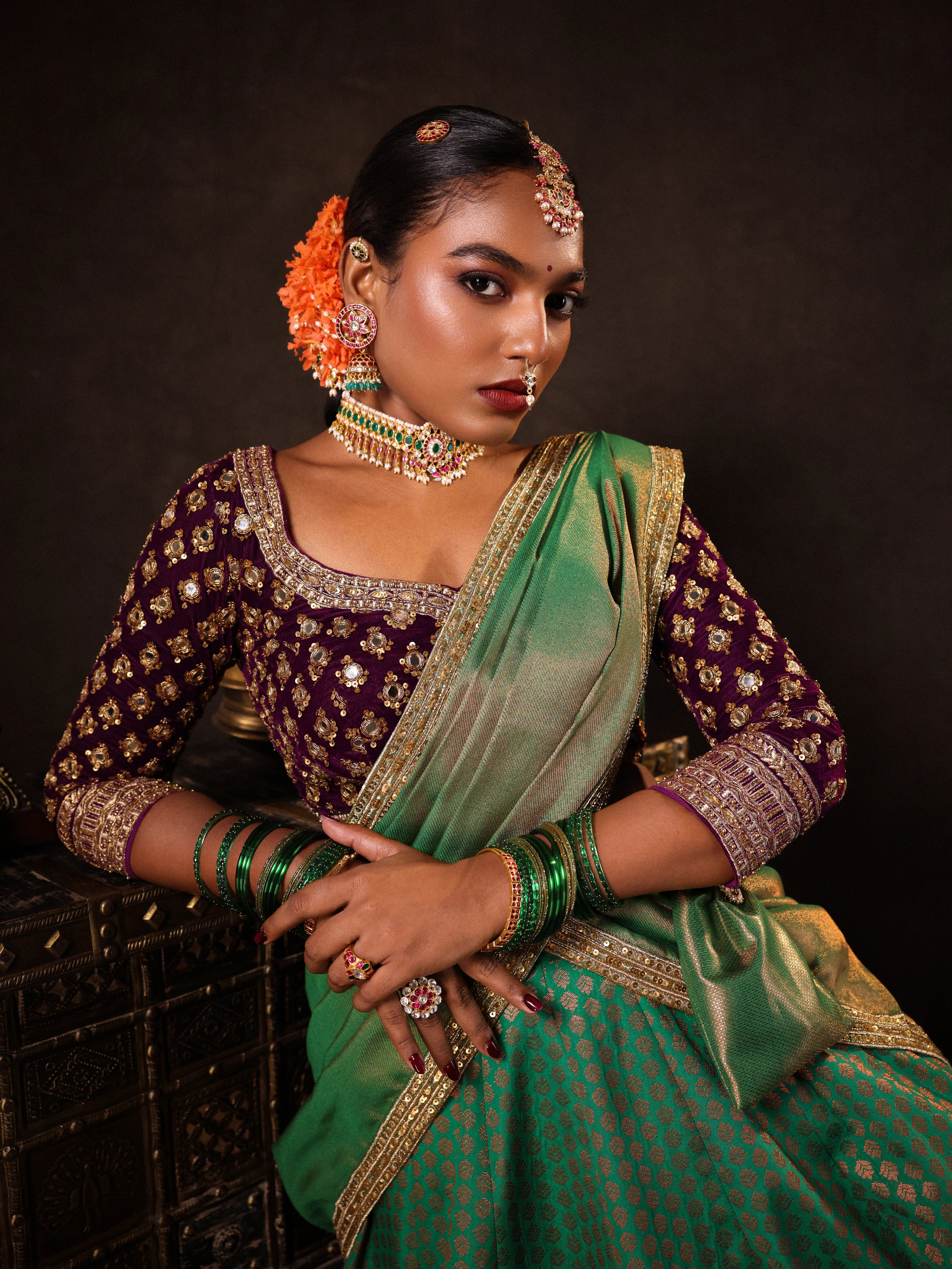 Model Ashika Crystal posing in a green and purple half saree set with a velvet blouse, tissue silk dupatta and brocade skirt handcrafted with zardozi, mirror, zari, cutdana and sequins. Team Archana Karthick completed the style with green glass bangles, a ring, a choker, jhumkas, nose ring and a maang tikka.
