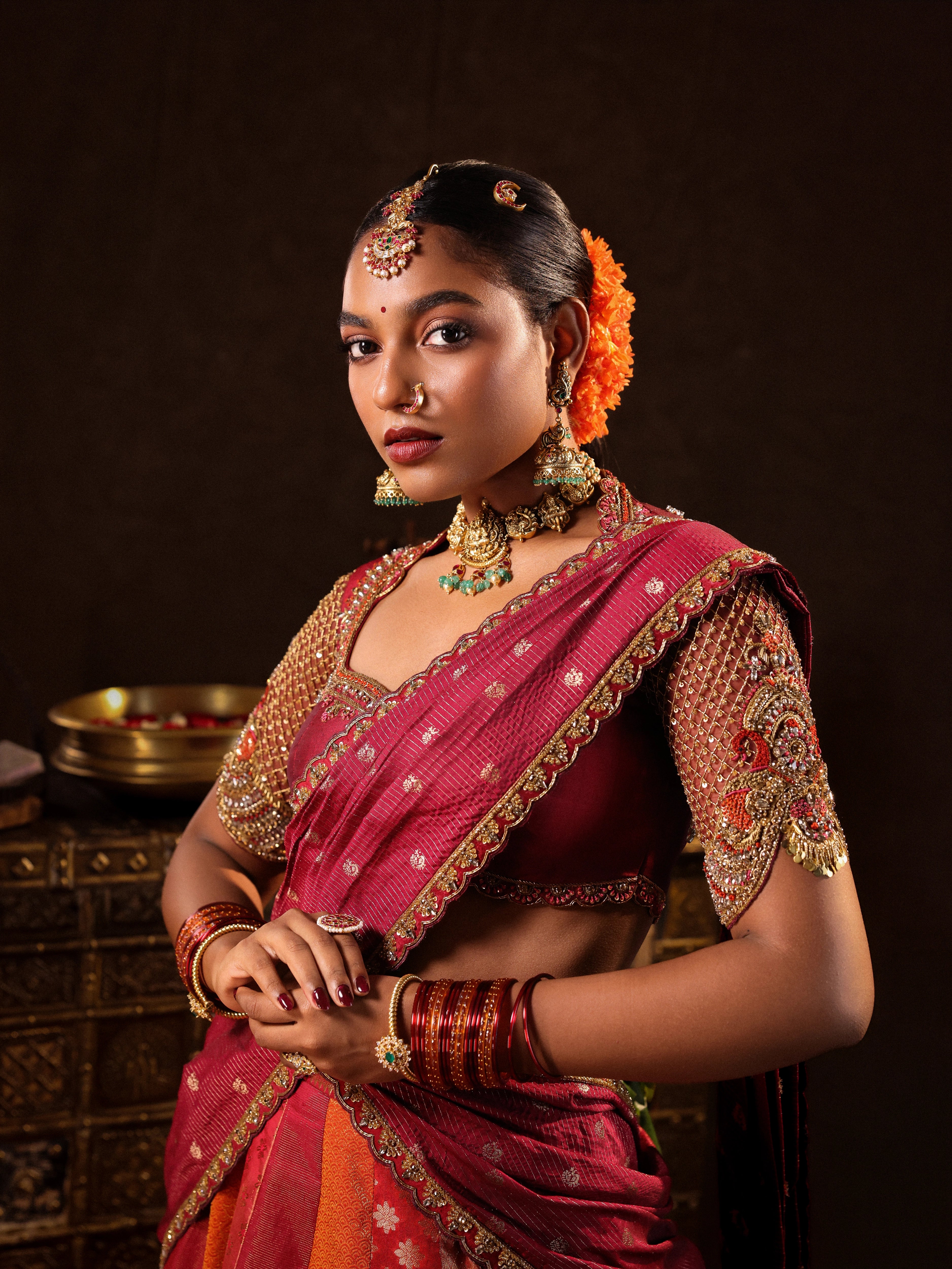 Model Ashika Crystal posing in a red and orange silk half saree with a scalloped veil is handrcrafted with sequins, cutdana, resham, stones and exquisite hangings. Team Archana Karthick completed the style with orange & red glass bangles, a ring, jhumkas, nose ring and a maang tikka.