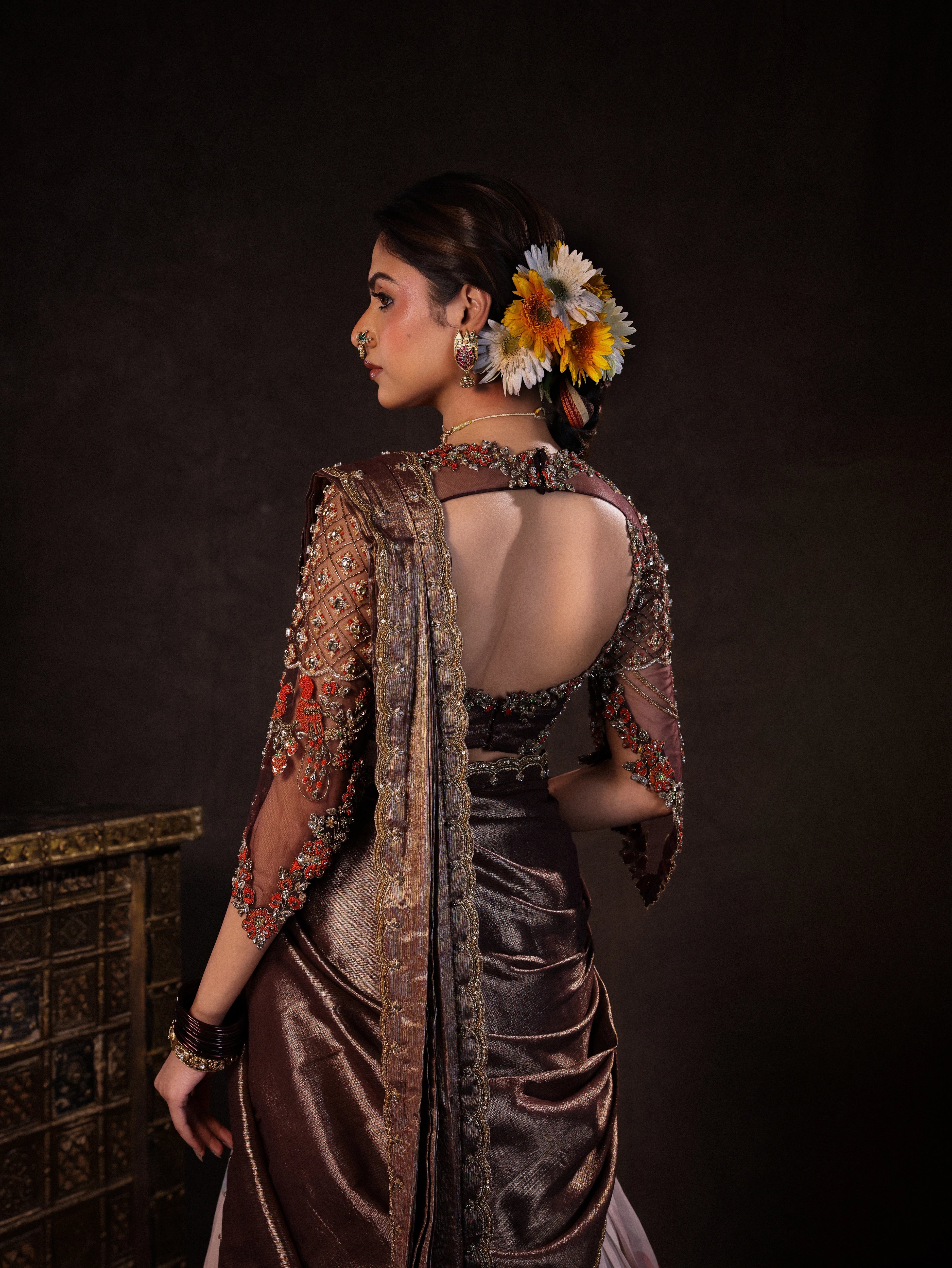 Model Dr Sree Advaita posing for back blouse design in a brown & printed ivory silk half saree set handcrafted with zardozi, resham, cutdana, sequins & rhinestones. Team Archana Karthick completed the style with brown glass bangles, a ring, jhumkas, nose ring and a maang tikka.